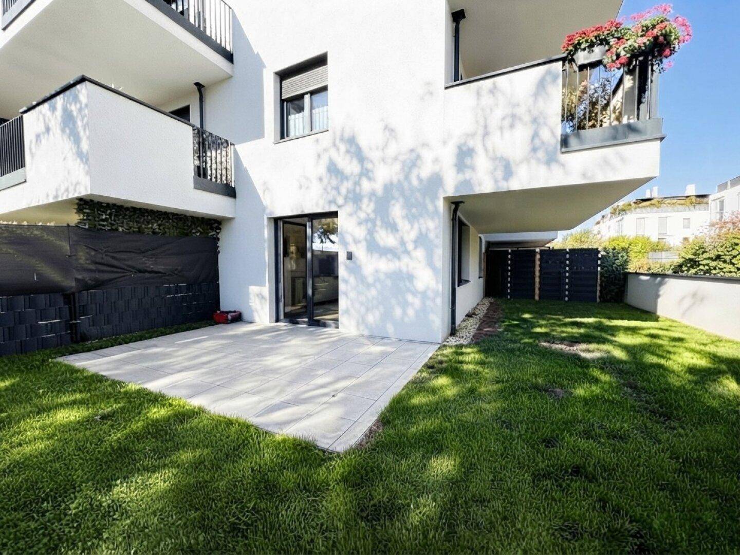 Außenbereich mit Terrasse und privatem Garten, umgeben von moderner Wohnbebauung.
