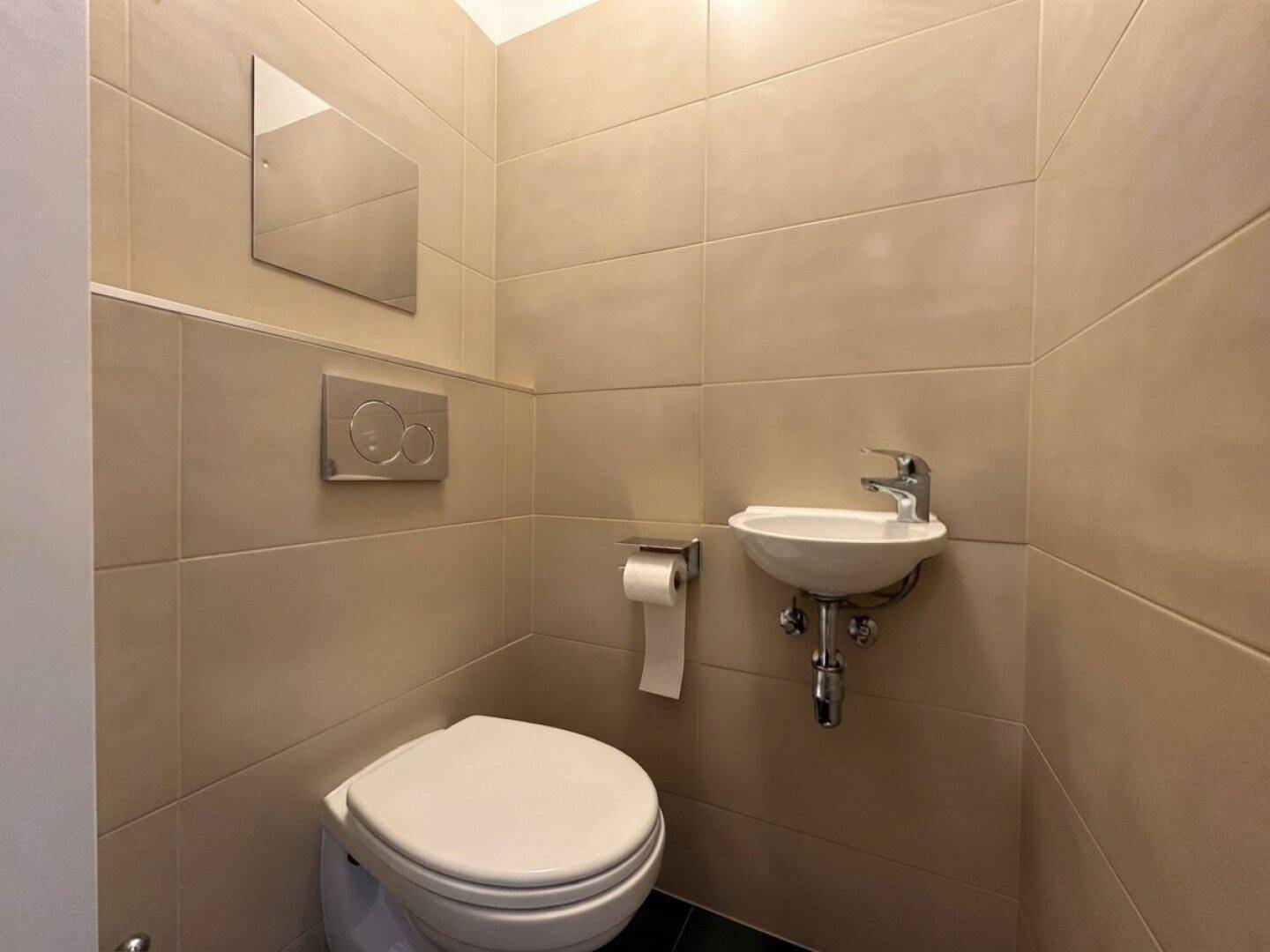 Kleines Gäste-WC mit beigefarbenen Fliesen, Toilette und Handwaschbecken.