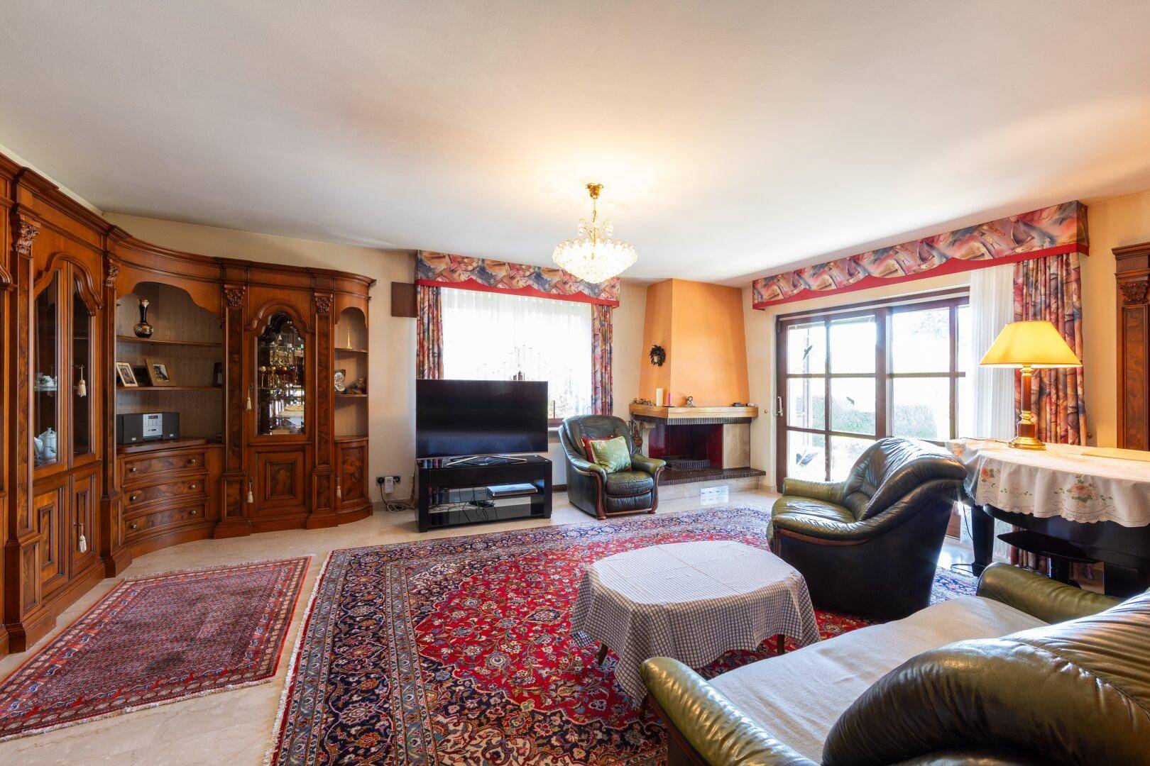Geräumiges Wohnzimmer mit traditionellen Holzmöbeln, Kamin und großem Orientteppich.