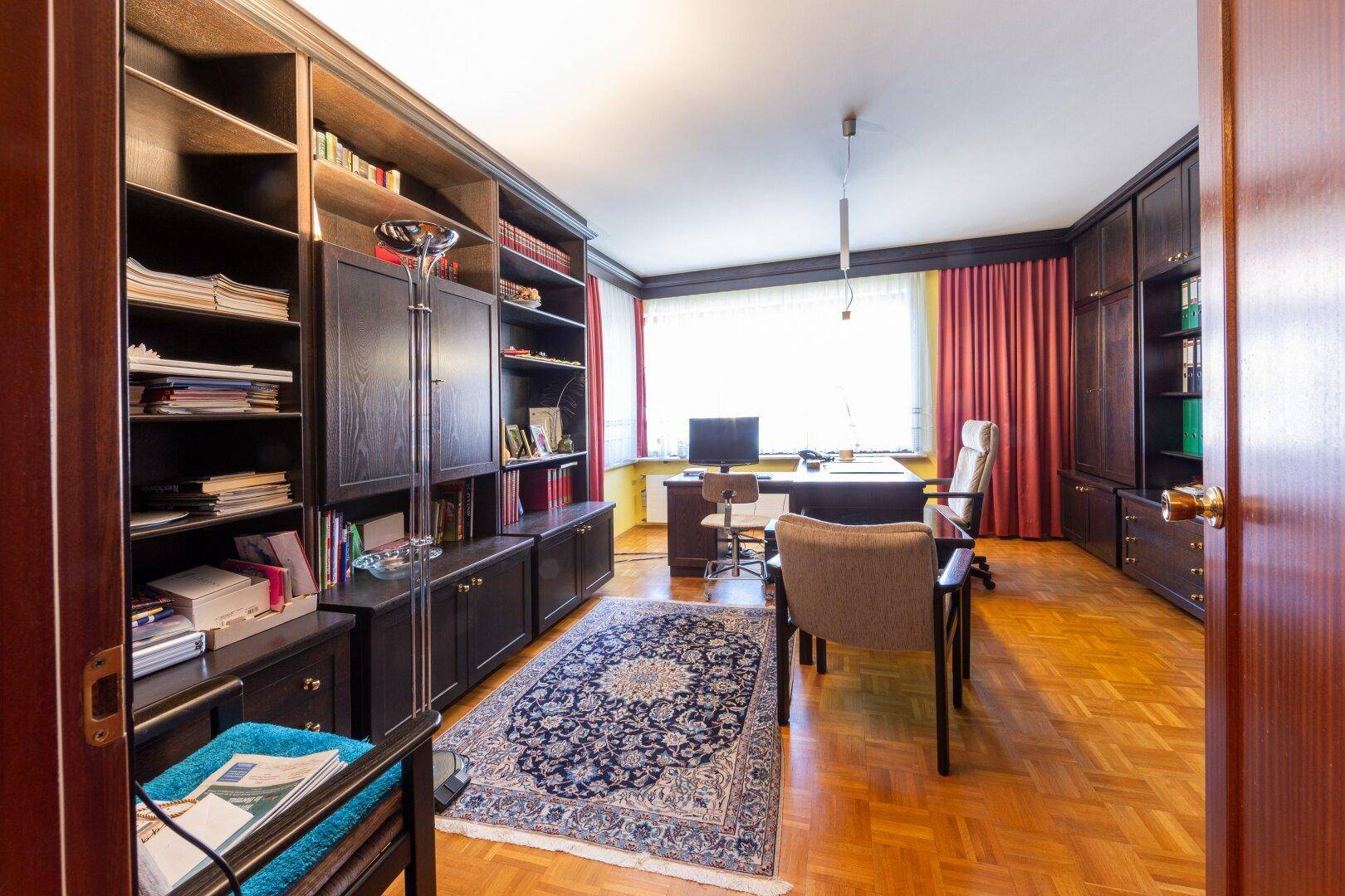 Helles Arbeitszimmer mit dunklen Holzregalen, Parkettboden und großem Fenster.