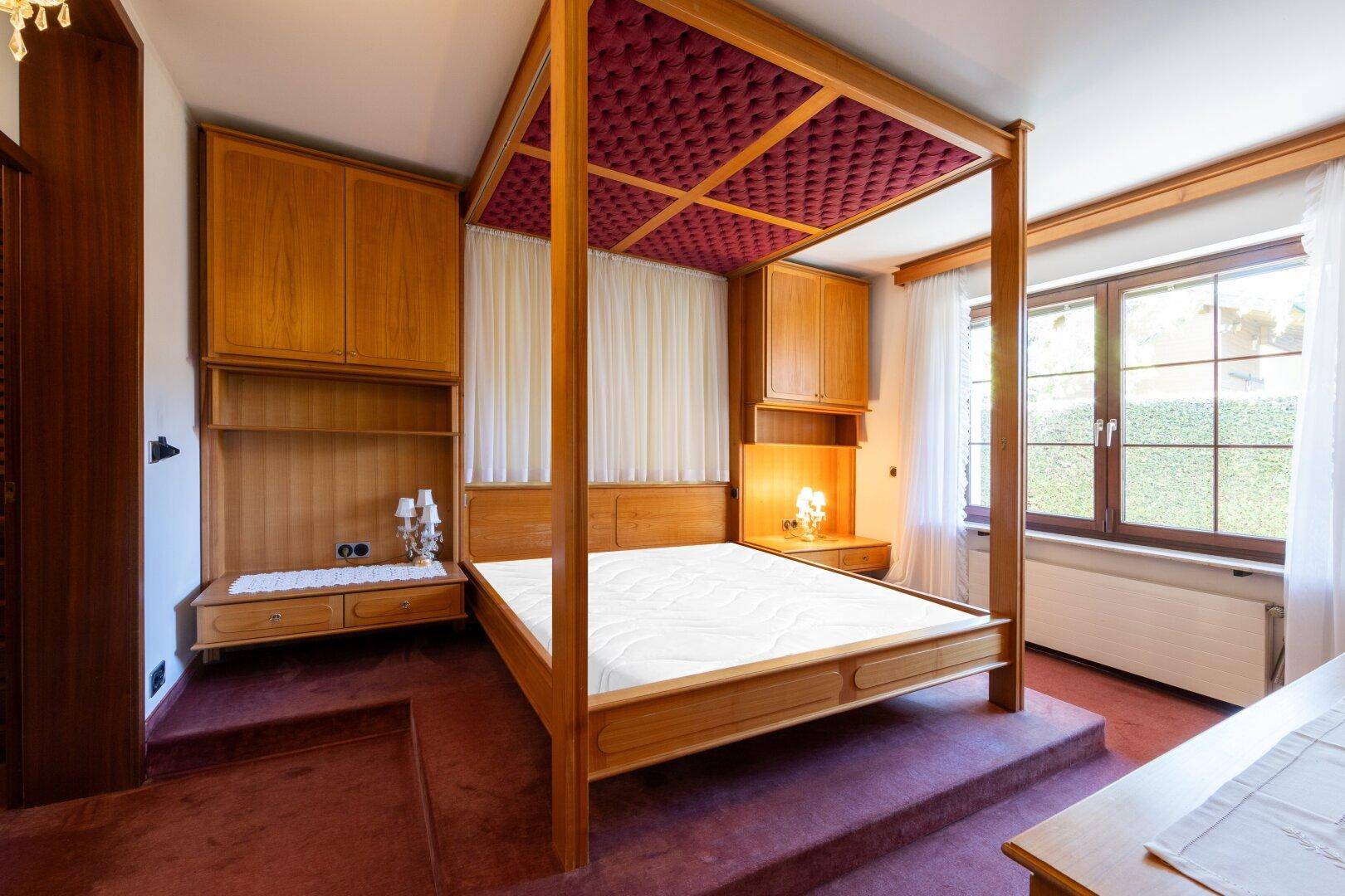 Schlafzimmer mit Himmelbett, integrierten Holzschränken und Teppichboden in warmen Farben.