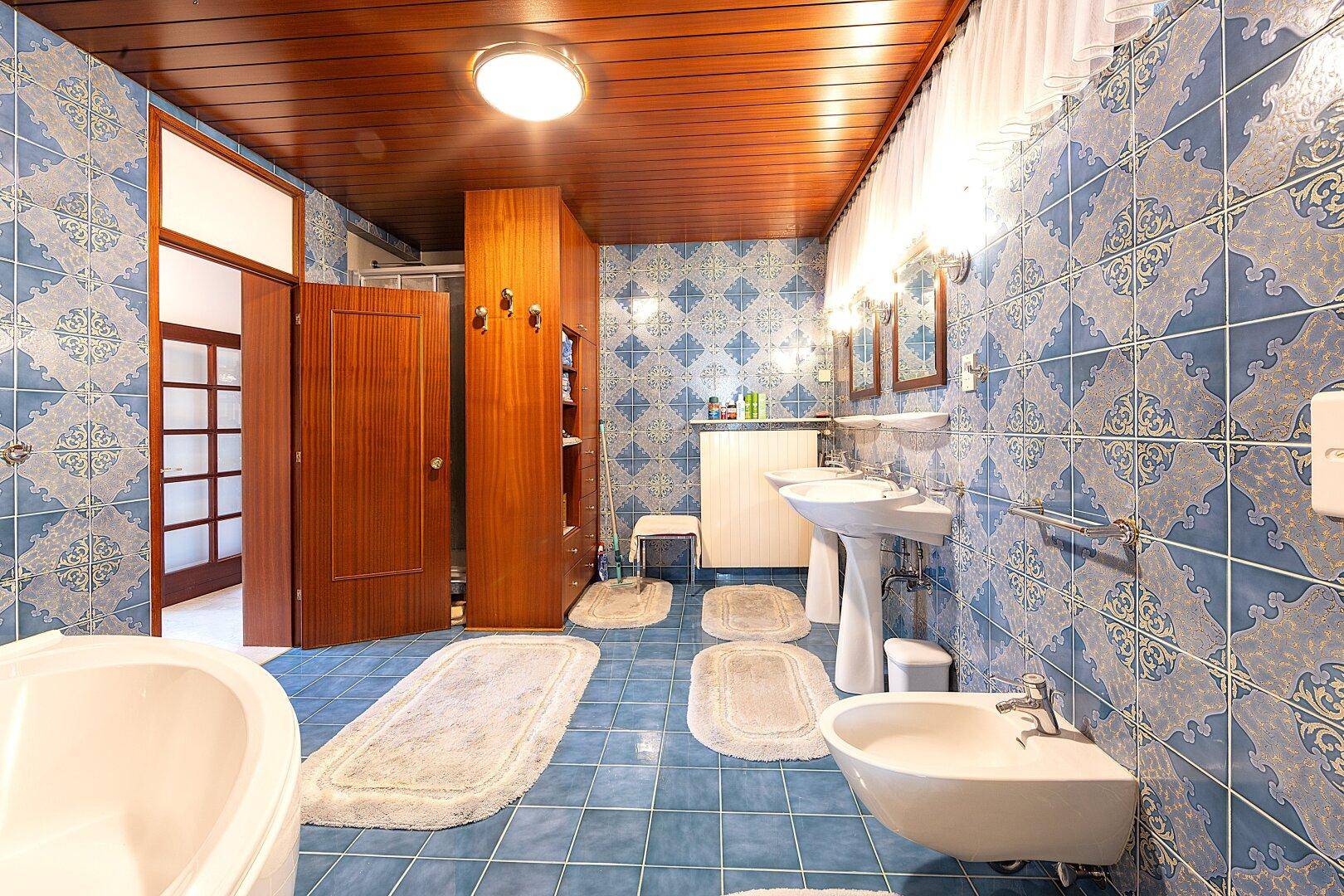 Geräumiges Badezimmer mit blauen Fliesen, Doppelwaschbecken und Holzdecke.