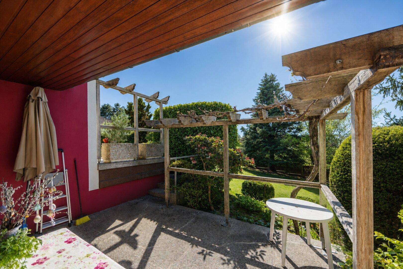 Sonniger Terrassenbereich mit Pergola, Sitzgelegenheiten und Blick in den grünen Garten.