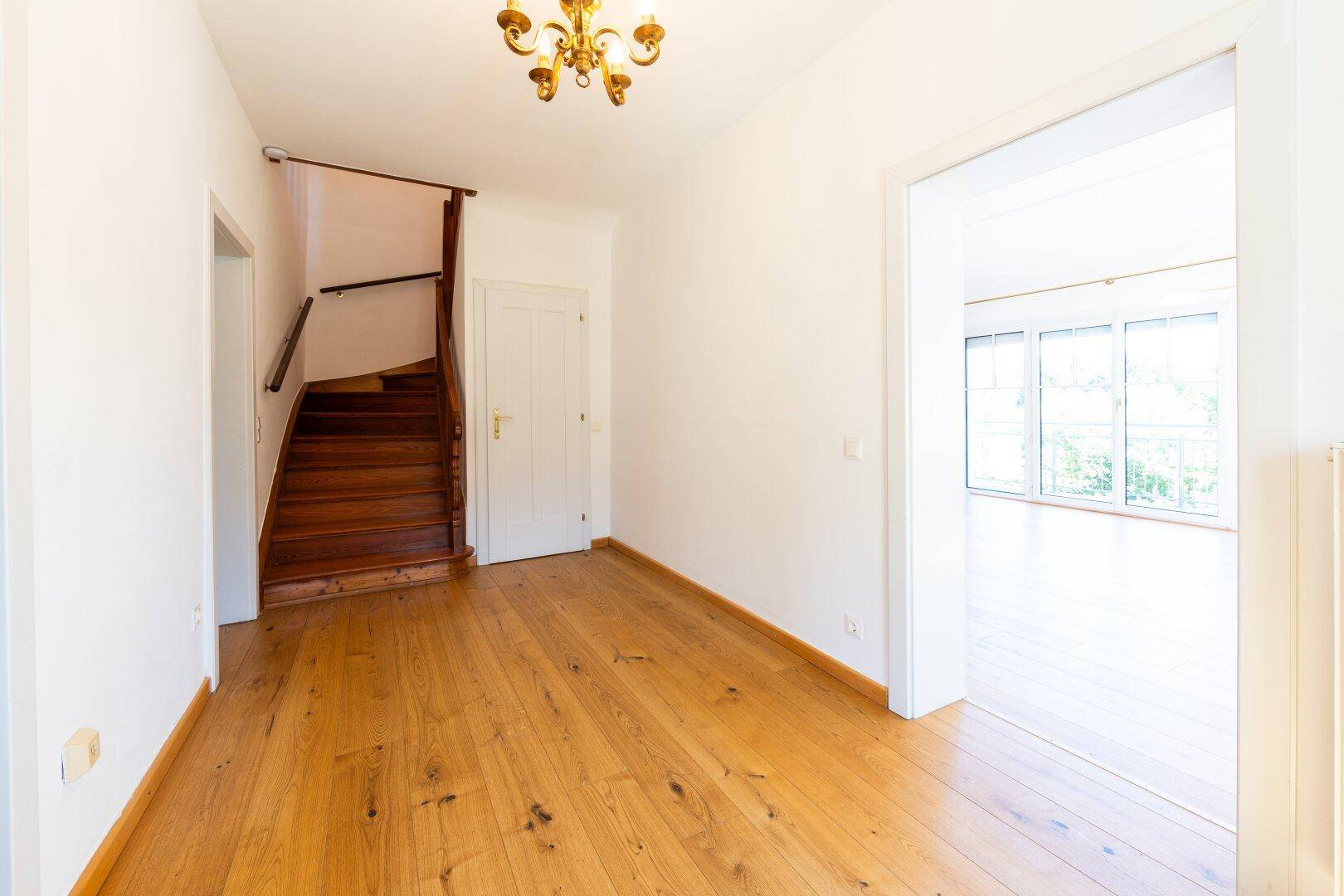 Heller Flur mit Holztreppe, Holzboden und Zugang zu weiteren Räumen im Haus.