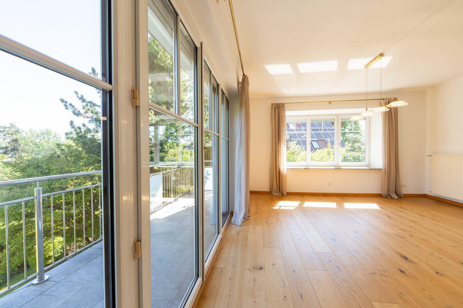 Geräumiges Wohnzimmer mit Holzboden, großen Fenstern und direktem Zugang zum Balkon.