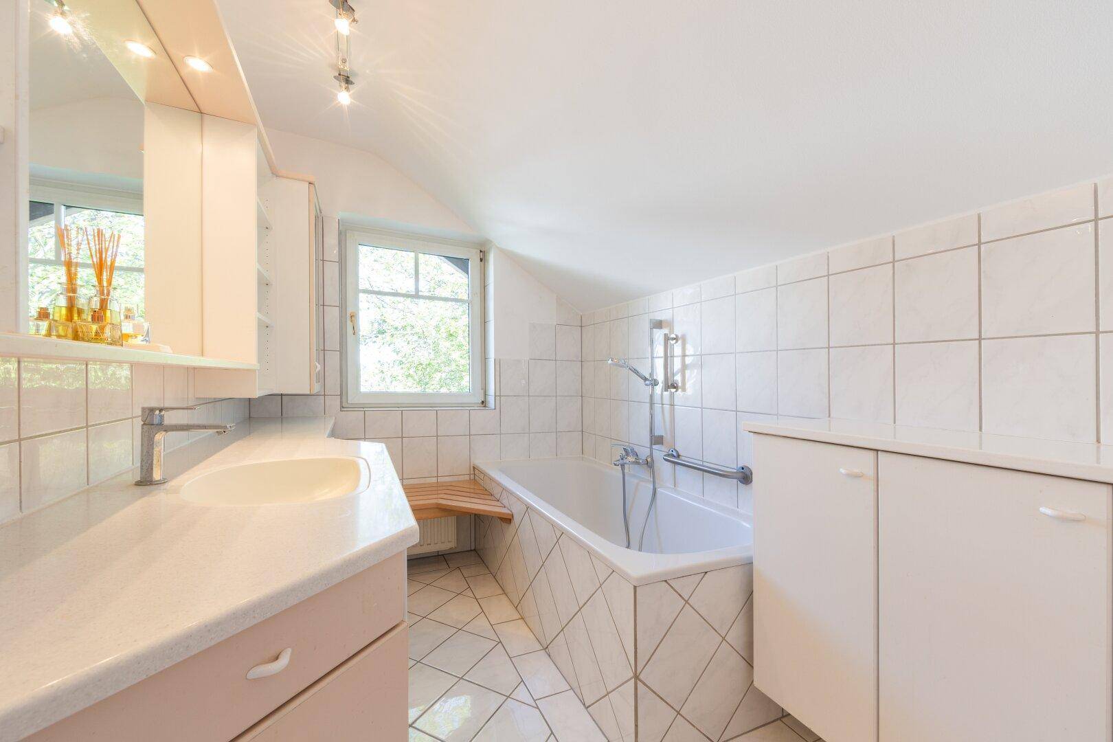 Gefliestes Badezimmer mit Badewanne, Waschbecken und Fenster für natürliche Belüftung.