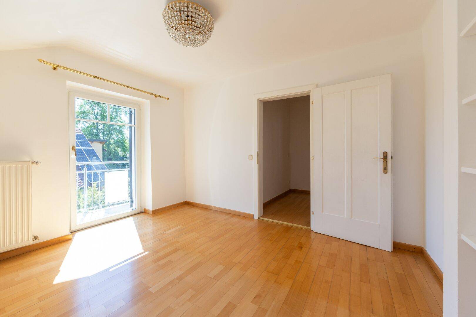 Helles Schlafzimmer mit Holzboden, Balkonzugang und Kronleuchter für eine elegante Atmosphäre.