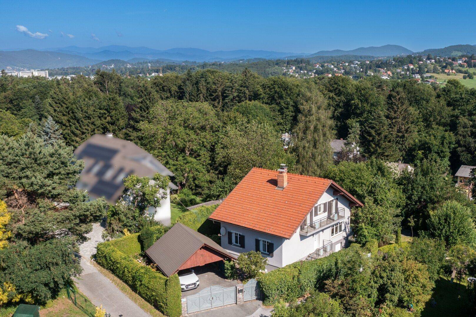 Weitläufige Luftaufnahme des Hauses in grüner Umgebung mit Blick auf die Stadt in der Ferne.