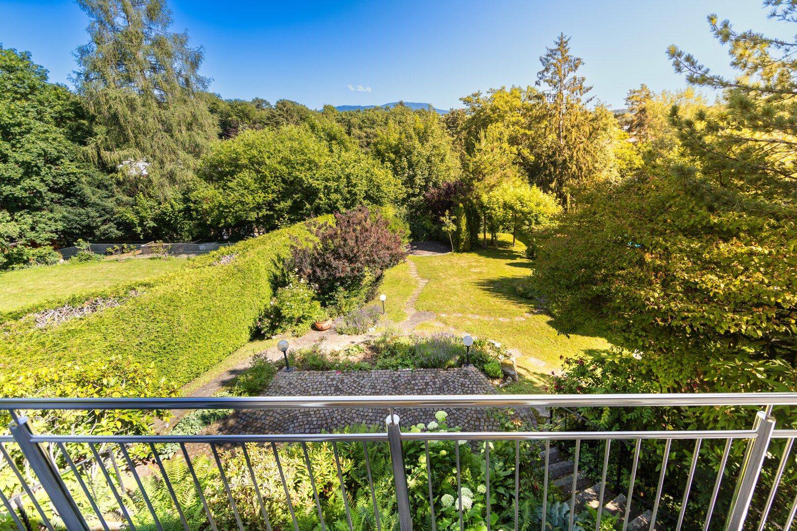 Weitläufiger Blick vom Balkon über den grünen Garten und die umliegende bewaldete Landschaft.