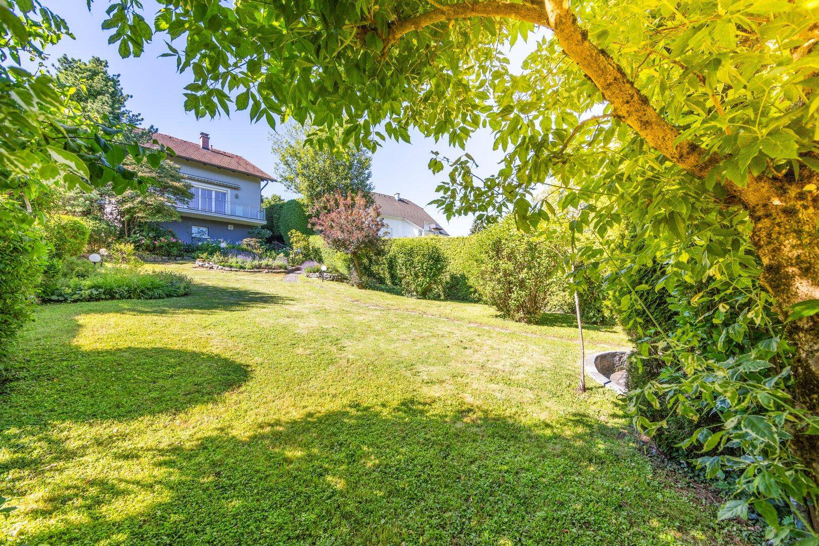 Großer, gepflegter Garten mit Rasenfläche und üppiger Bepflanzung unter strahlendem Sonnenschein.