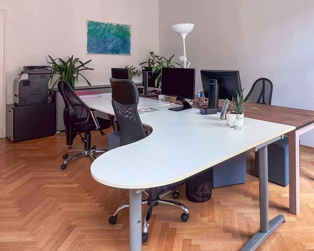 Geräumiges Büro mit mehreren Arbeitsplätzen, Computern und Pflanzen auf dem Fischgrätparkettboden.