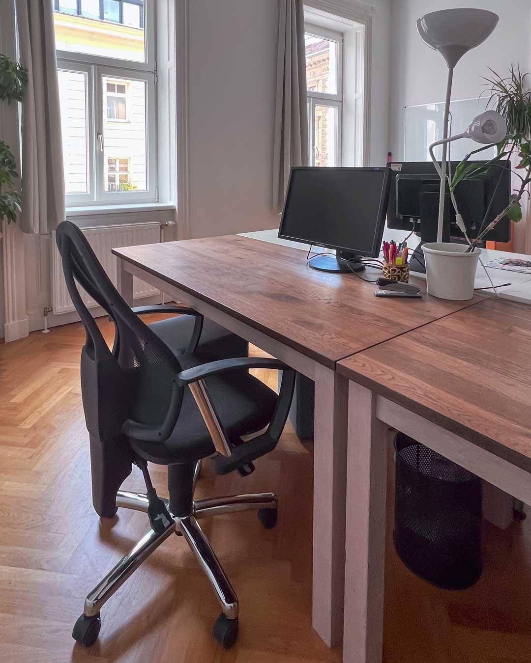 Detailansicht eines Arbeitsplatzes mit Holzschreibtisch, Bürostuhl und Blick aus dem Fenster.