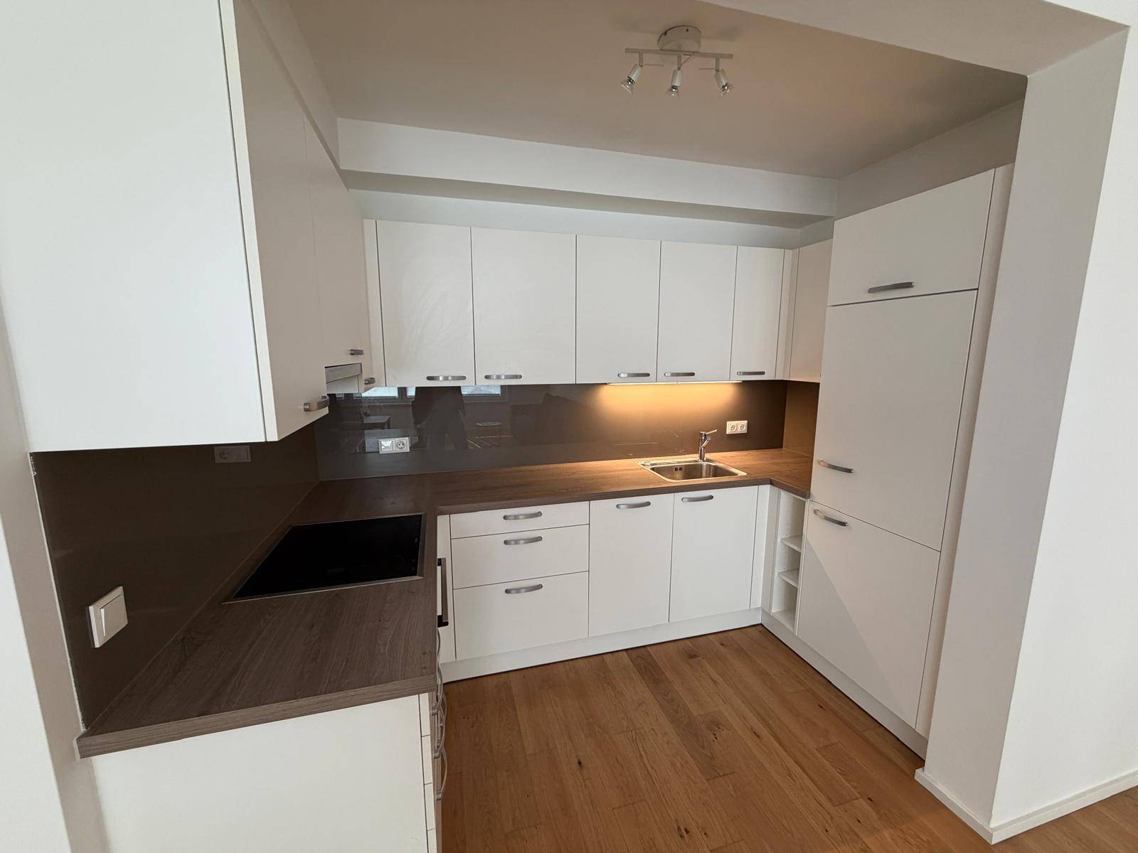 Moderne Einbauküche mit weißen Schränken, dunkler Arbeitsplatte und Induktionskochfeld.