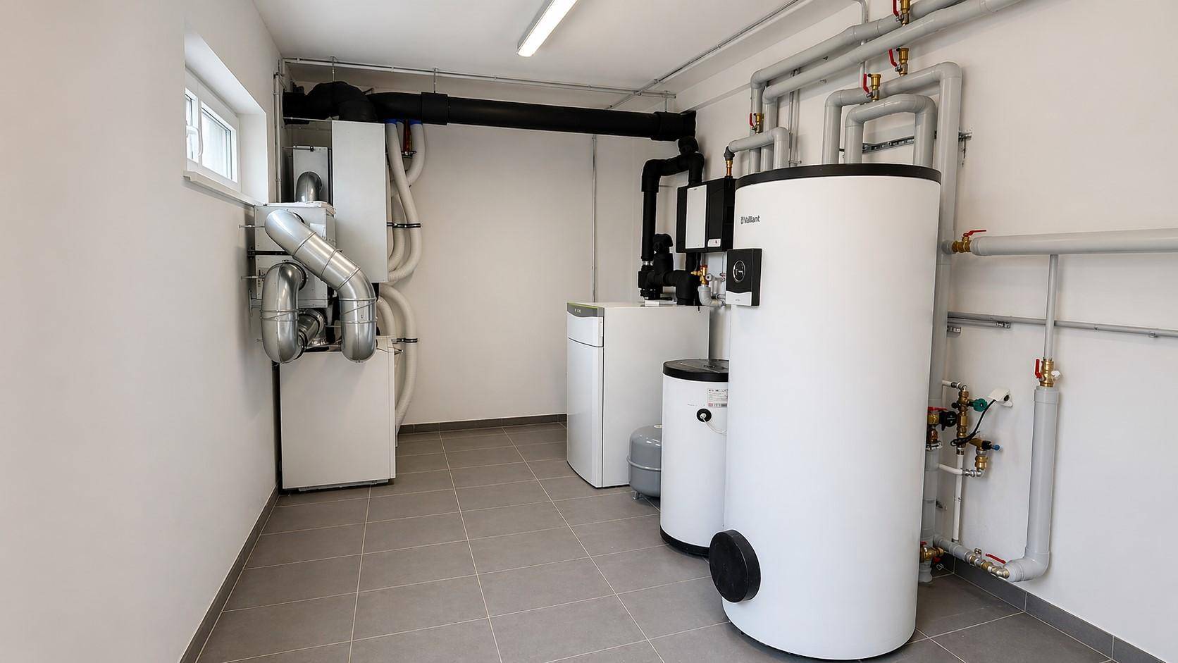 Technikraum mit Heizungsanlage, Warmwasserspeicher und sichtbaren Rohrleitungen.