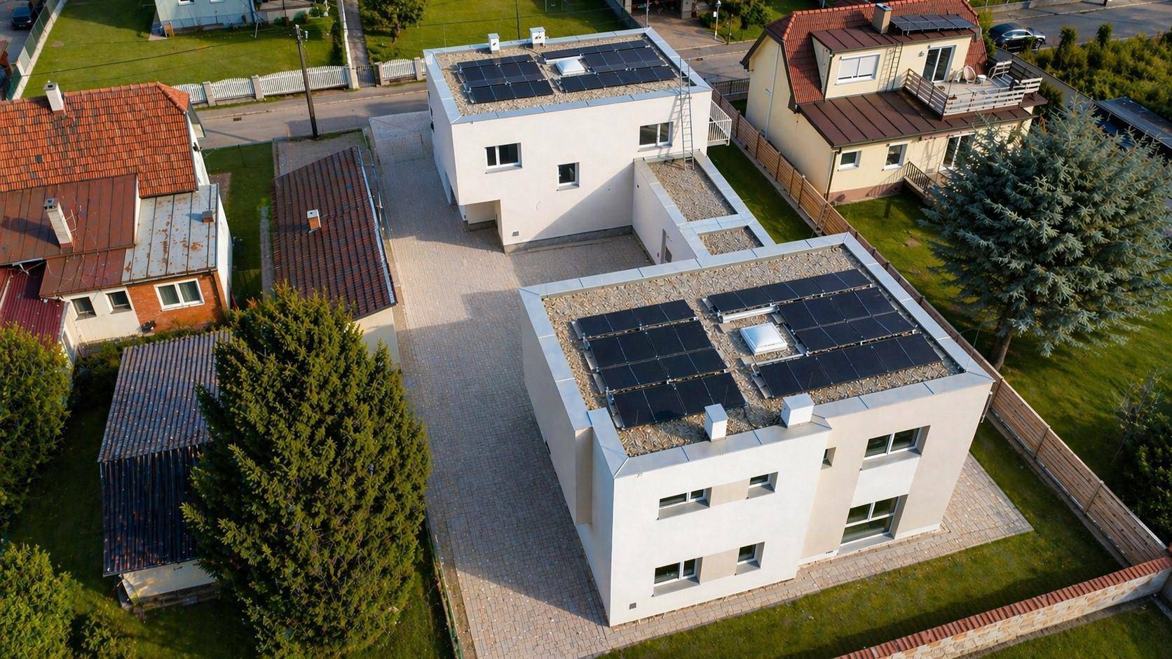 Weitläufige Luftaufnahme der beiden Neubauten mit Solarpaneelen auf den Dächern und umliegenden Gärten.