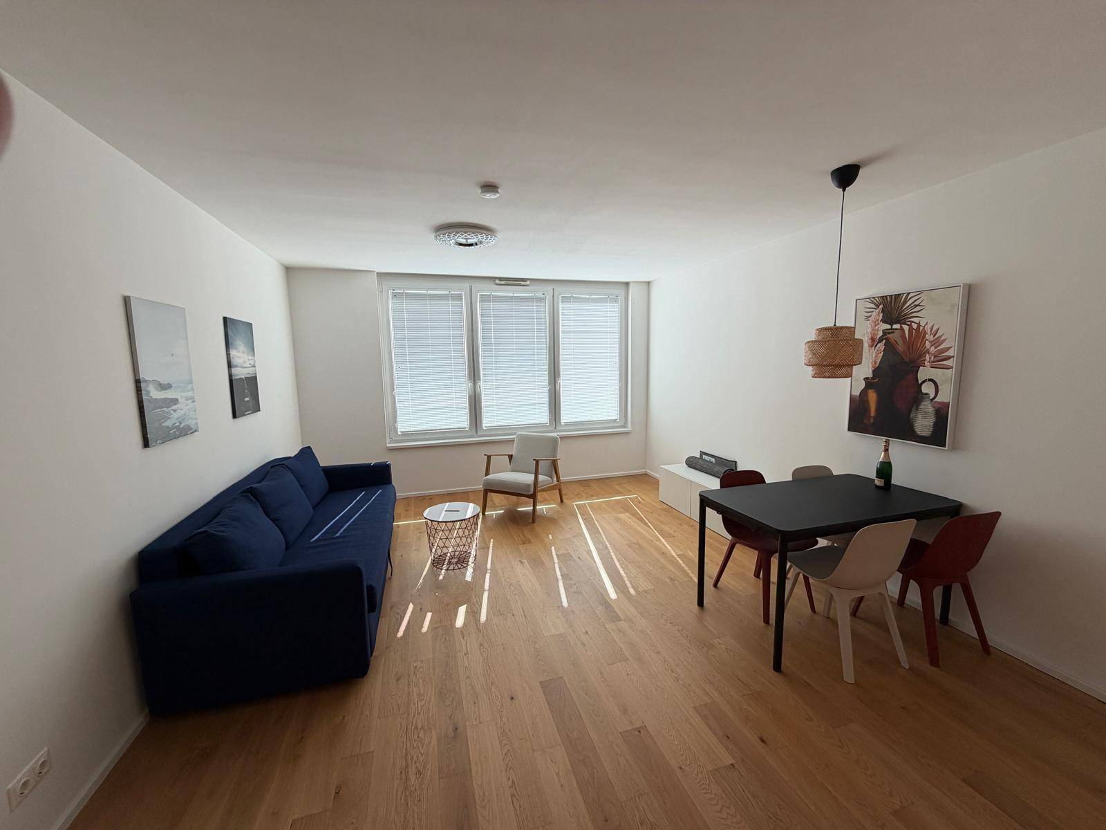 Heller Wohn- und Essbereich mit Holzboden, Sofa, Esstisch und großen Fenstern.