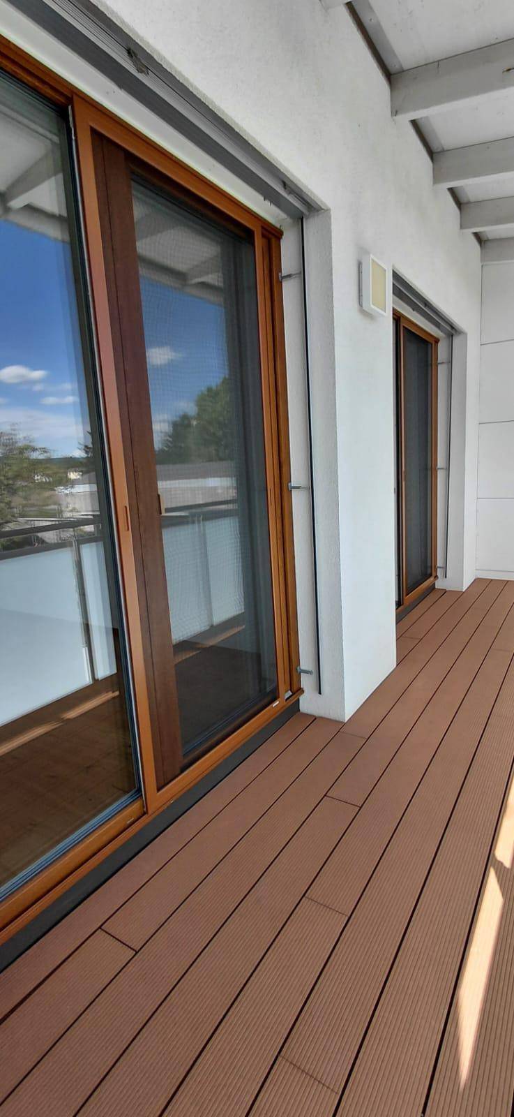 Geräumiger Balkon mit Holzboden und großen Schiebetüren, ideal für sonnige Stunden.