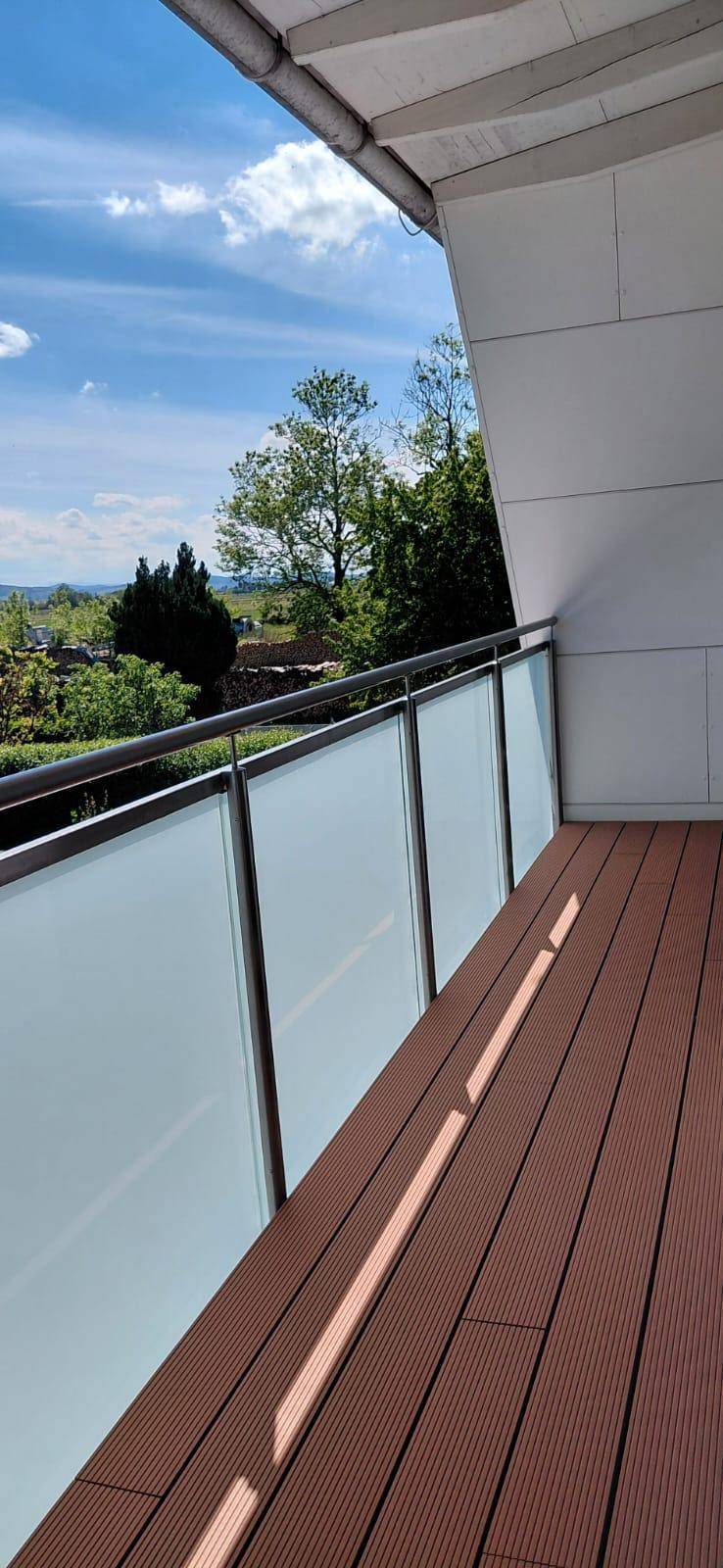 Heller Balkon mit Glasgeländer und weitem Blick ins Grüne, perfekt zum Entspannen.