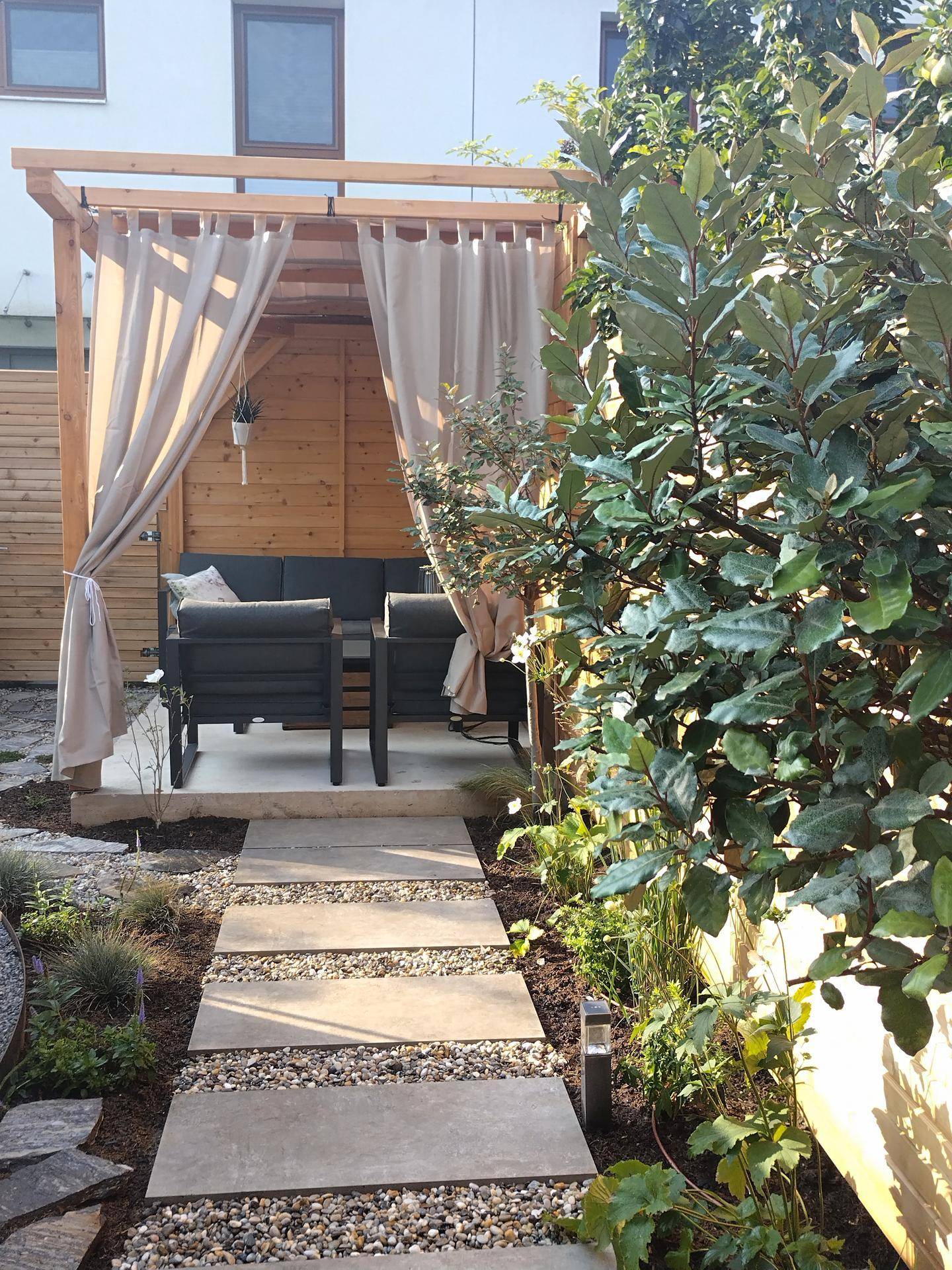 Idyllischer Gartenbereich mit Pergola, Vorhängen und gemütlicher Lounge-Sitzgruppe.