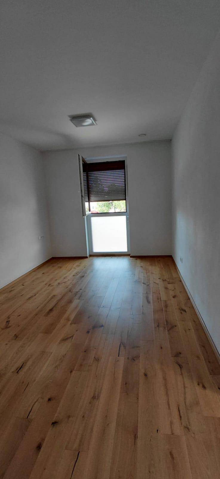 Helles Zimmer mit Holzboden und Fenster mit Rollladen, bereit zur individuellen Gestaltung.