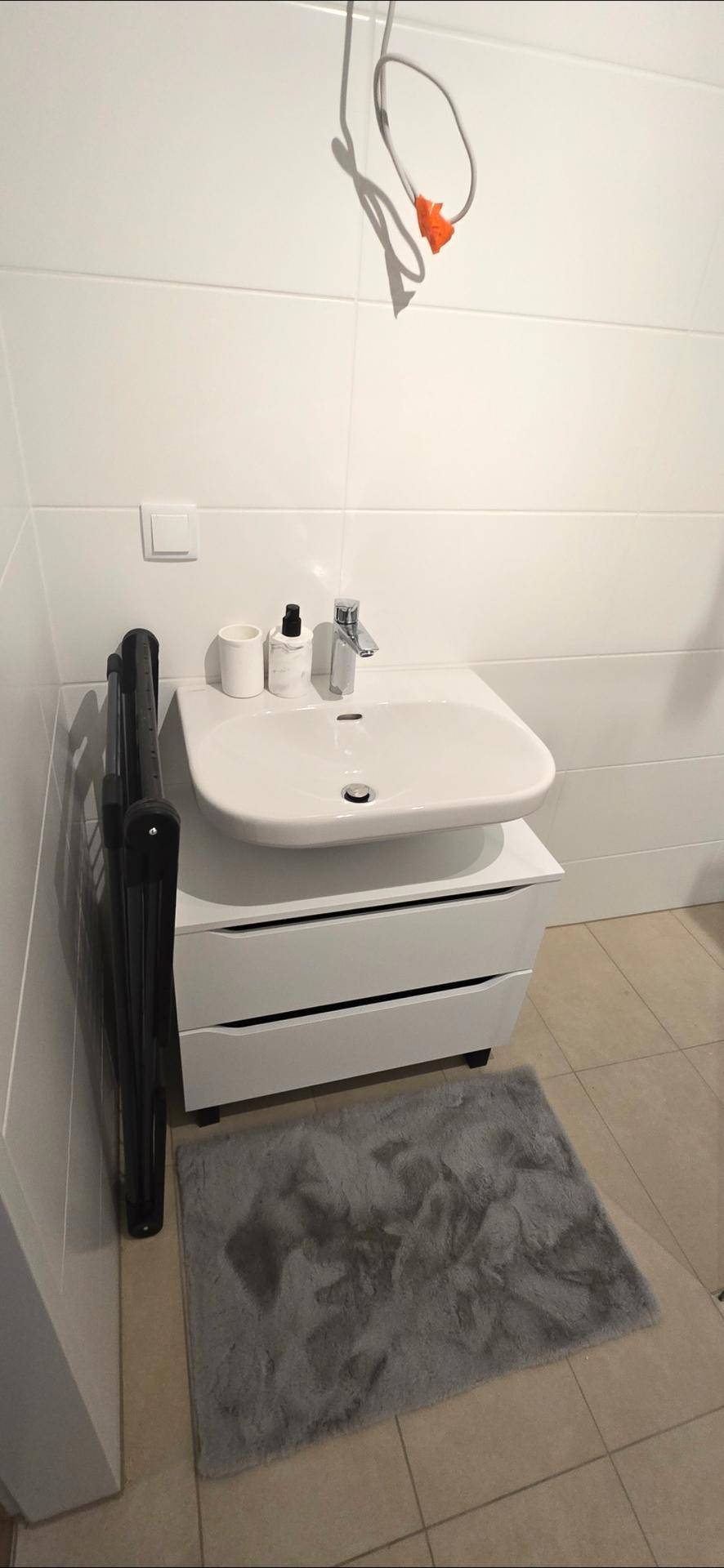 Waschbecken mit Unterschrank und Spiegel in einem hell gefliesten Badezimmer.