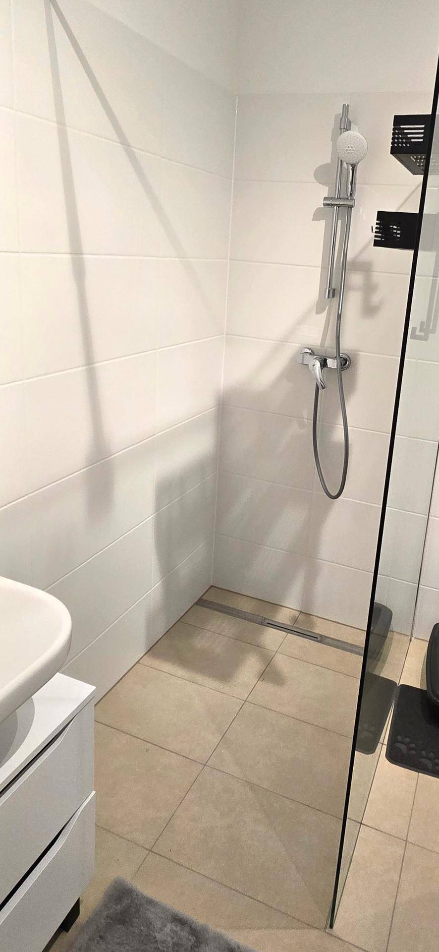 Modernes Badezimmer mit ebenerdiger Dusche und hellen Fliesen an Wänden und Boden.