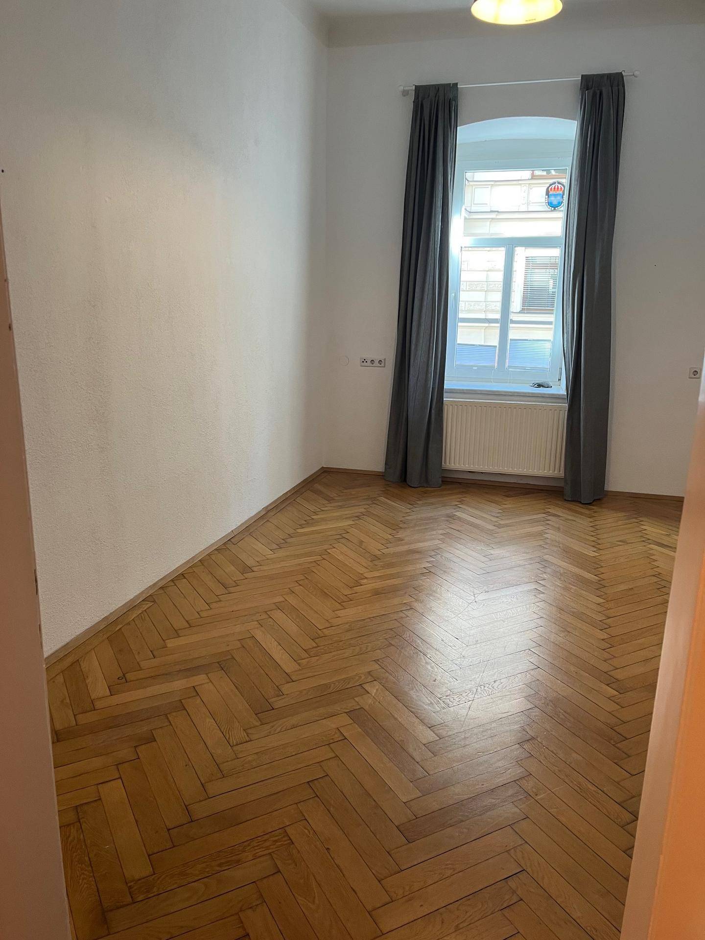 Helles Schlafzimmer mit klassischem Fischgrätparkett und einem großen Fenster.