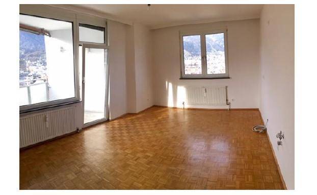 Helles Wohnzimmer mit Parkettboden, großen Fenstern und Zugang zu einem Balkon mit Bergblick.