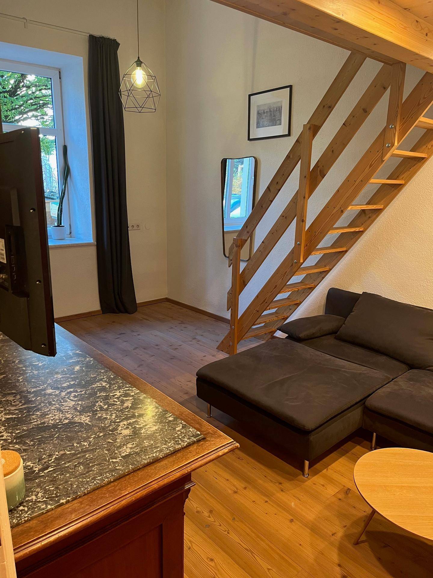 Wohnzimmer mit Holzboden, bequemer Couch und einer Holztreppe, die nach oben führt.