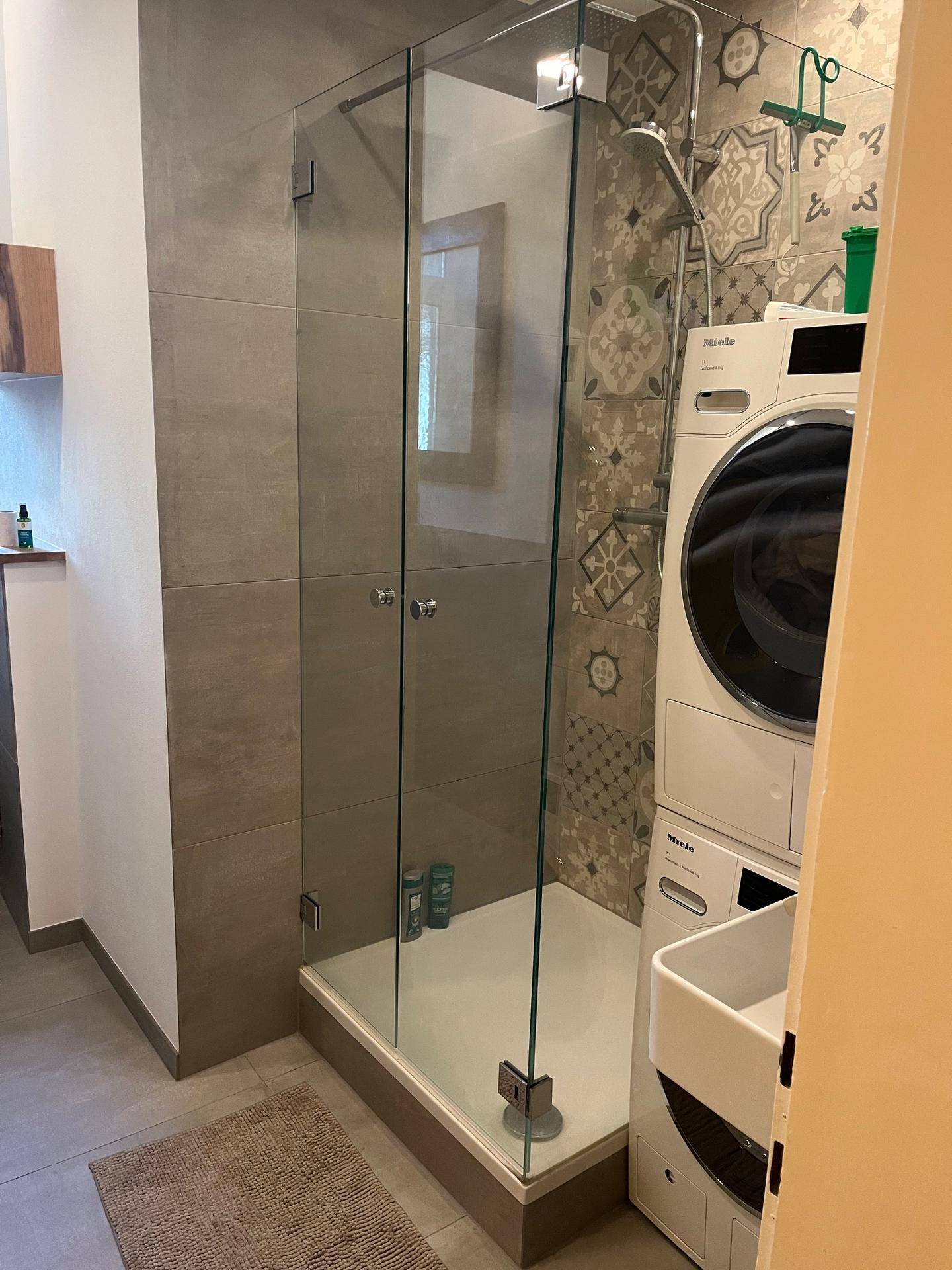 Modernes Badezimmer mit großer Glasdusche und integrierter Waschmaschine.