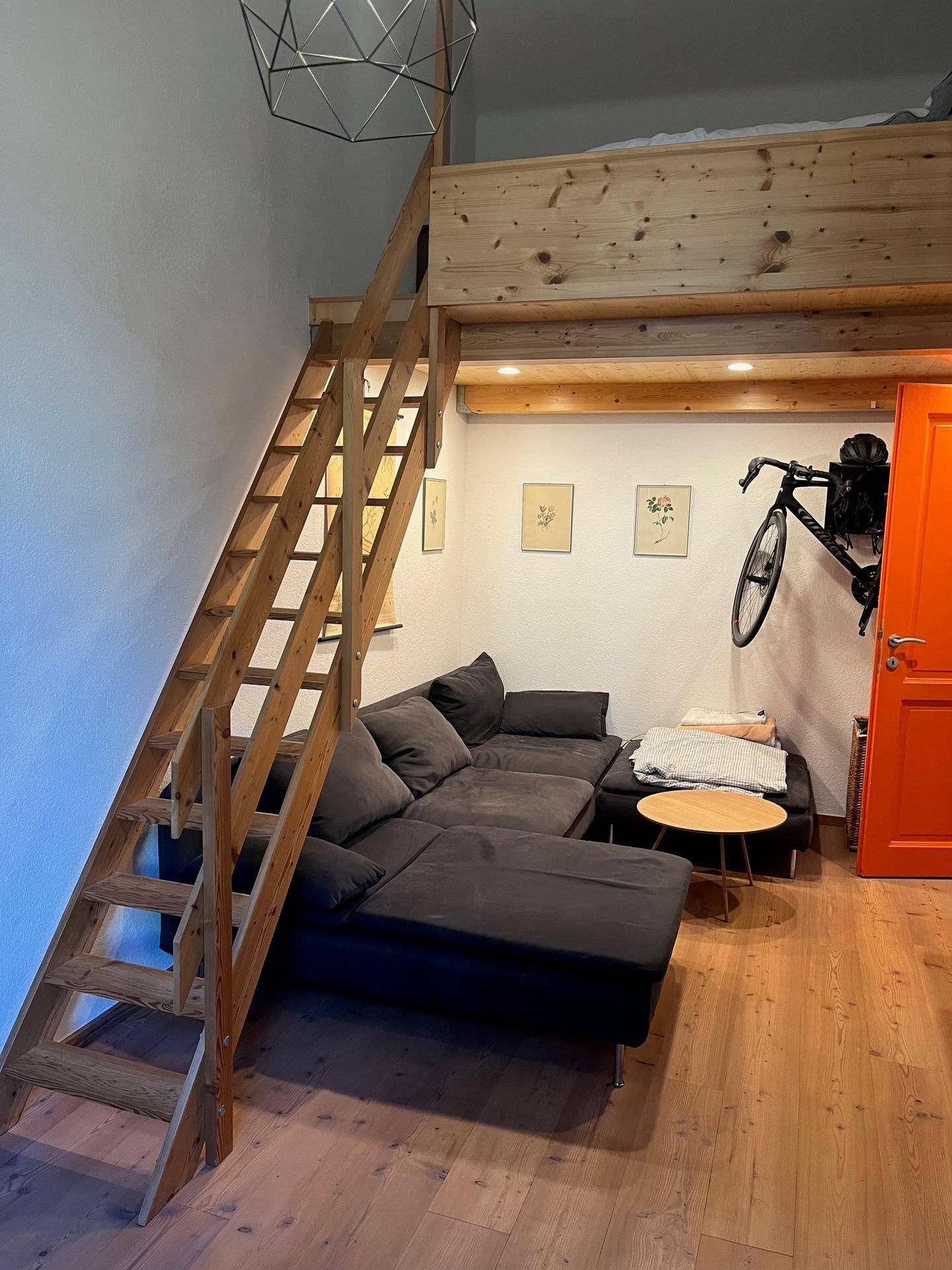 Gemütlicher Wohnbereich mit Sofa, Holztreppe zum Hochbett und moderner Beleuchtung.