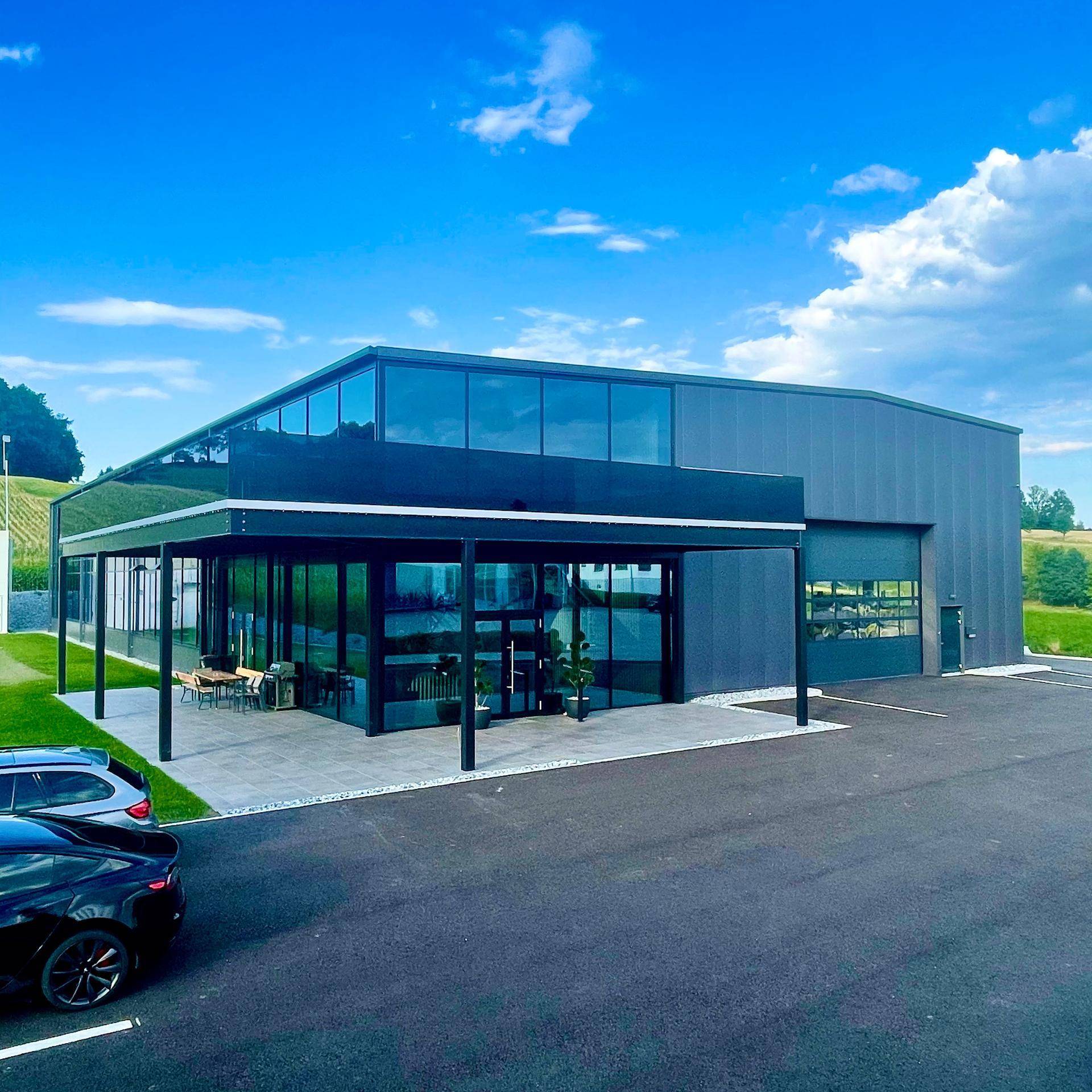 Ansicht des modernen Geschäftsgebäudes mit Glasfront und Parkplätzen im Vordergrund.