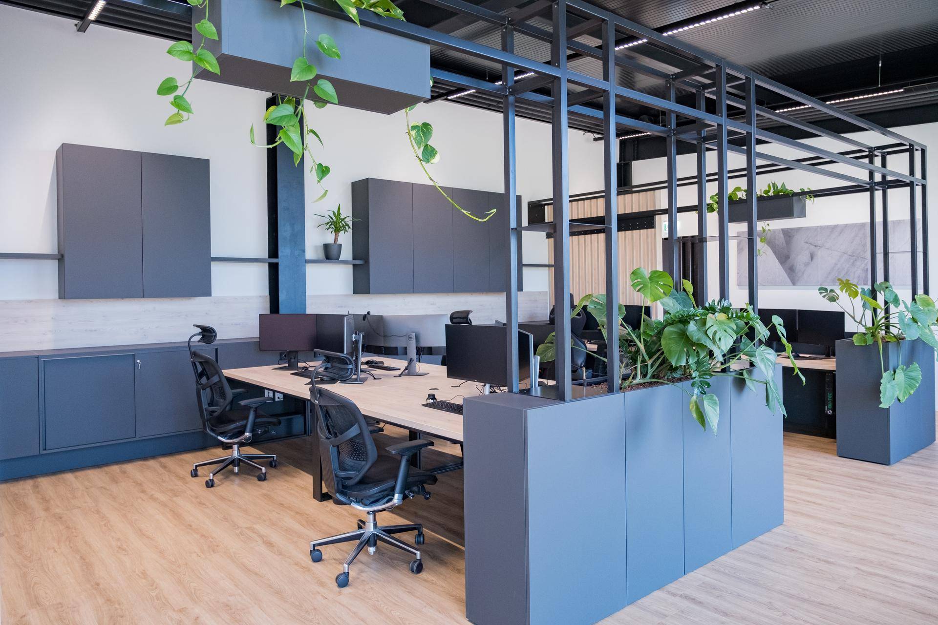 Helle Bürolandschaft mit ergonomischen Stühlen, Schreibtischen und integrierten Pflanzen.
