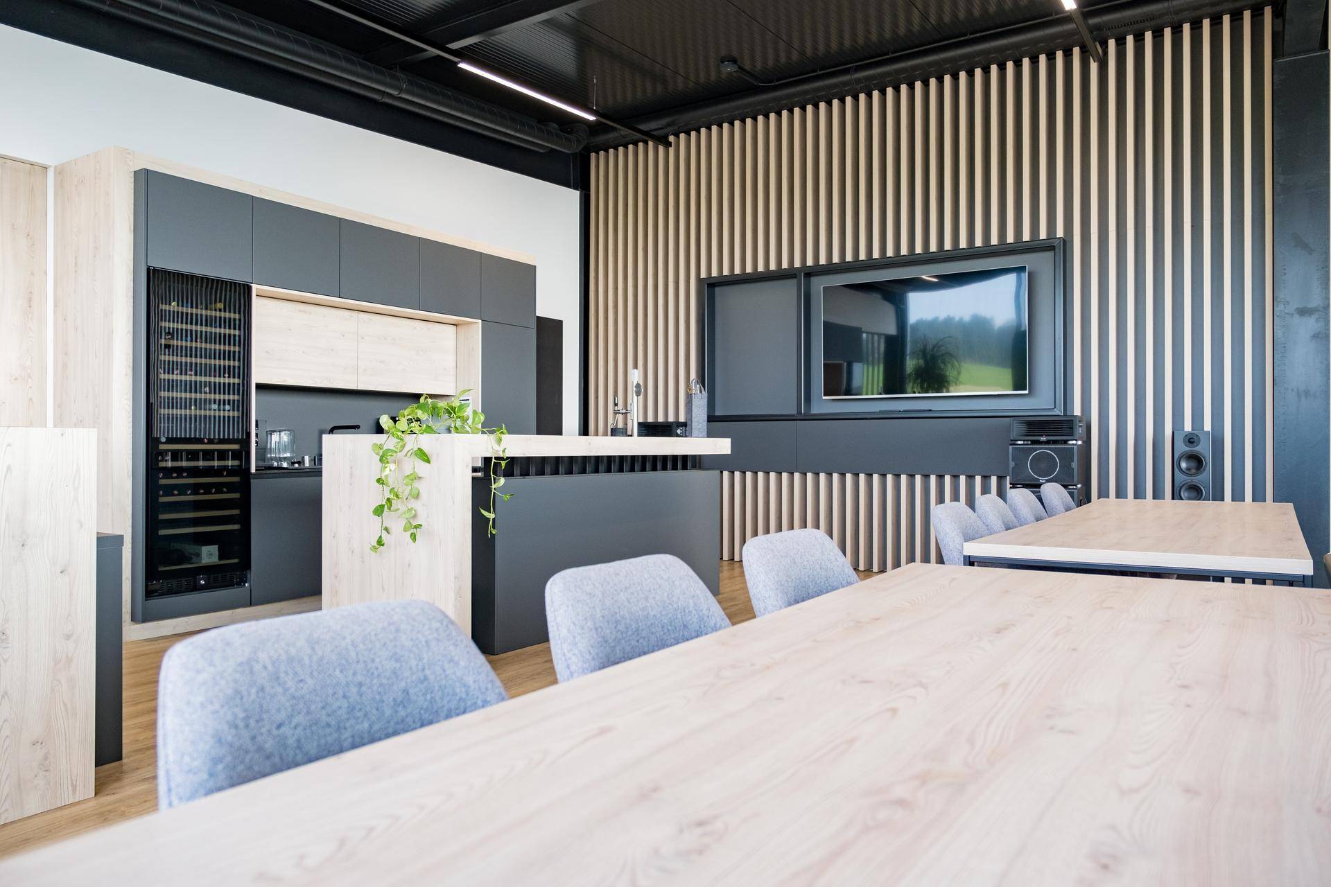 Moderner Küchen- und Essbereich mit Holzelementen, grauen Stühlen und großem Fernseher.