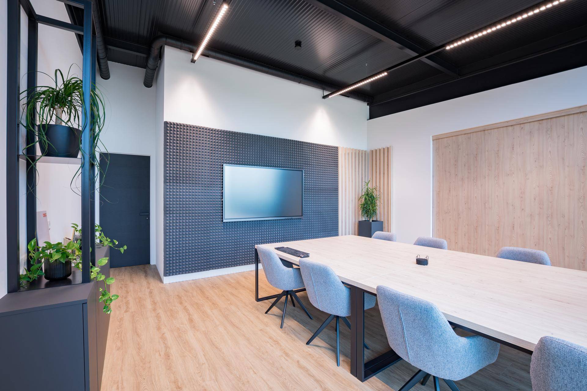 Konferenzraum mit modernem Design, großem Bildschirm und schallabsorbierender Wand.