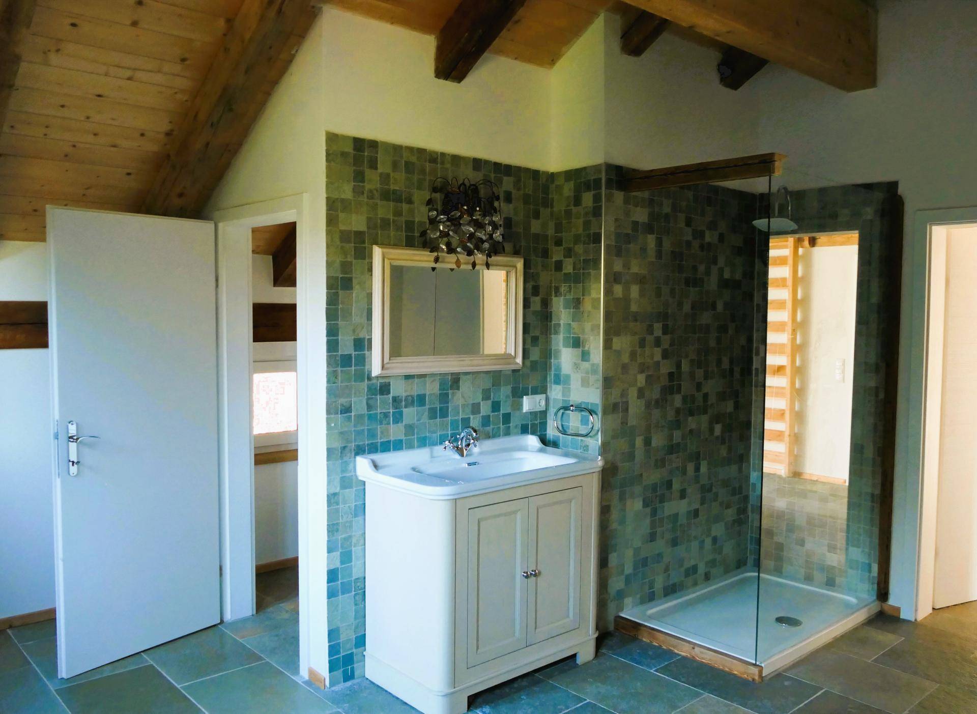 Modernes Badezimmer mit Duschkabine, Waschtisch und grünen Mosaikfliesen an der Wand.