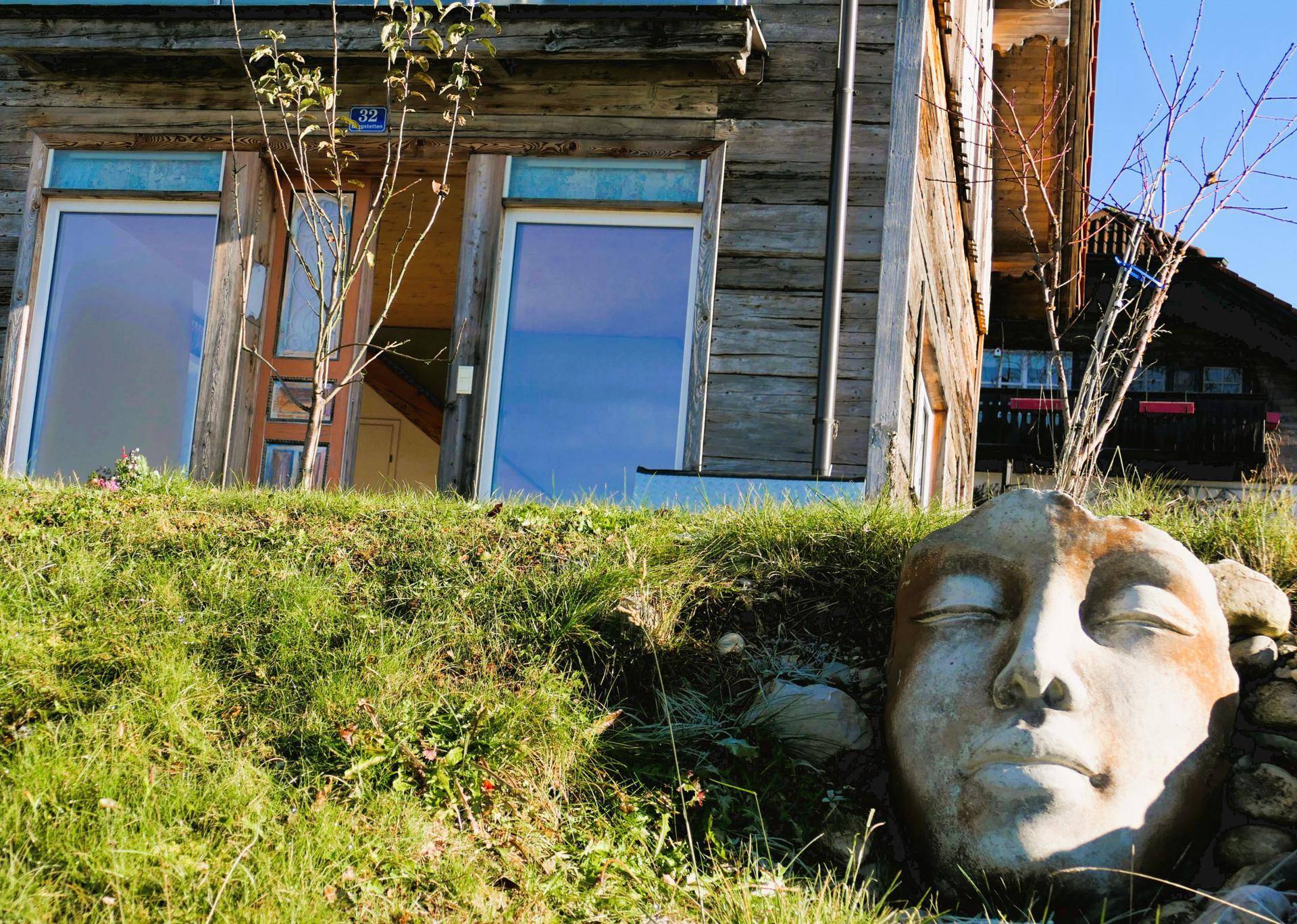 Detailansicht der Holzfassade mit großen Fenstern und einer dekorativen Steinskulptur im Vordergrund.