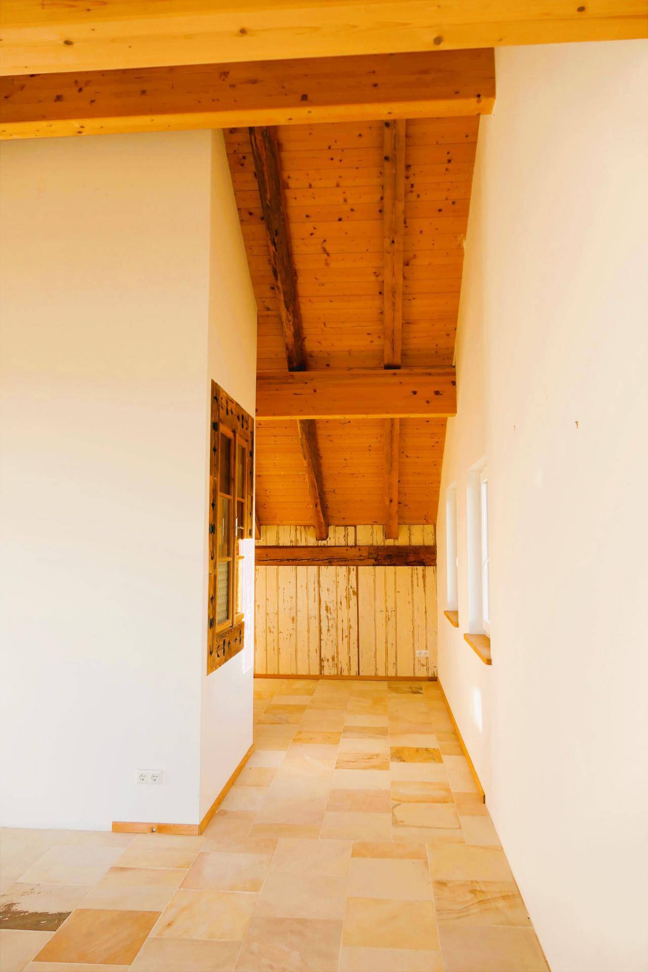 Heller Flur mit Holzbalkendecke, Fliesenboden und einem Fenster mit dekorativem Holzrahmen.