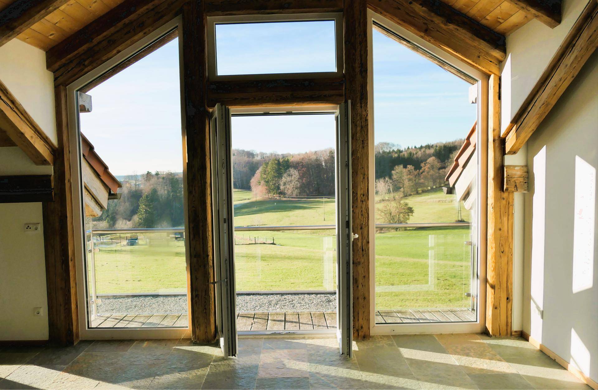 Lichtdurchfluteter Raum mit großen Glasfronten, Holzbalken und weitem Blick über die Landschaft.