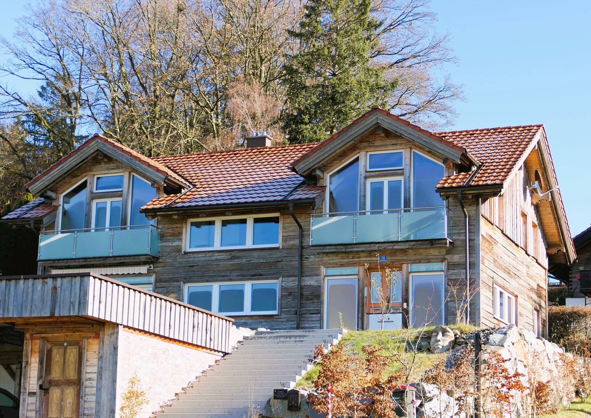Charmantes Holzhaus mit traditionellem Dach und großen Glasfronten, umgeben von Natur.