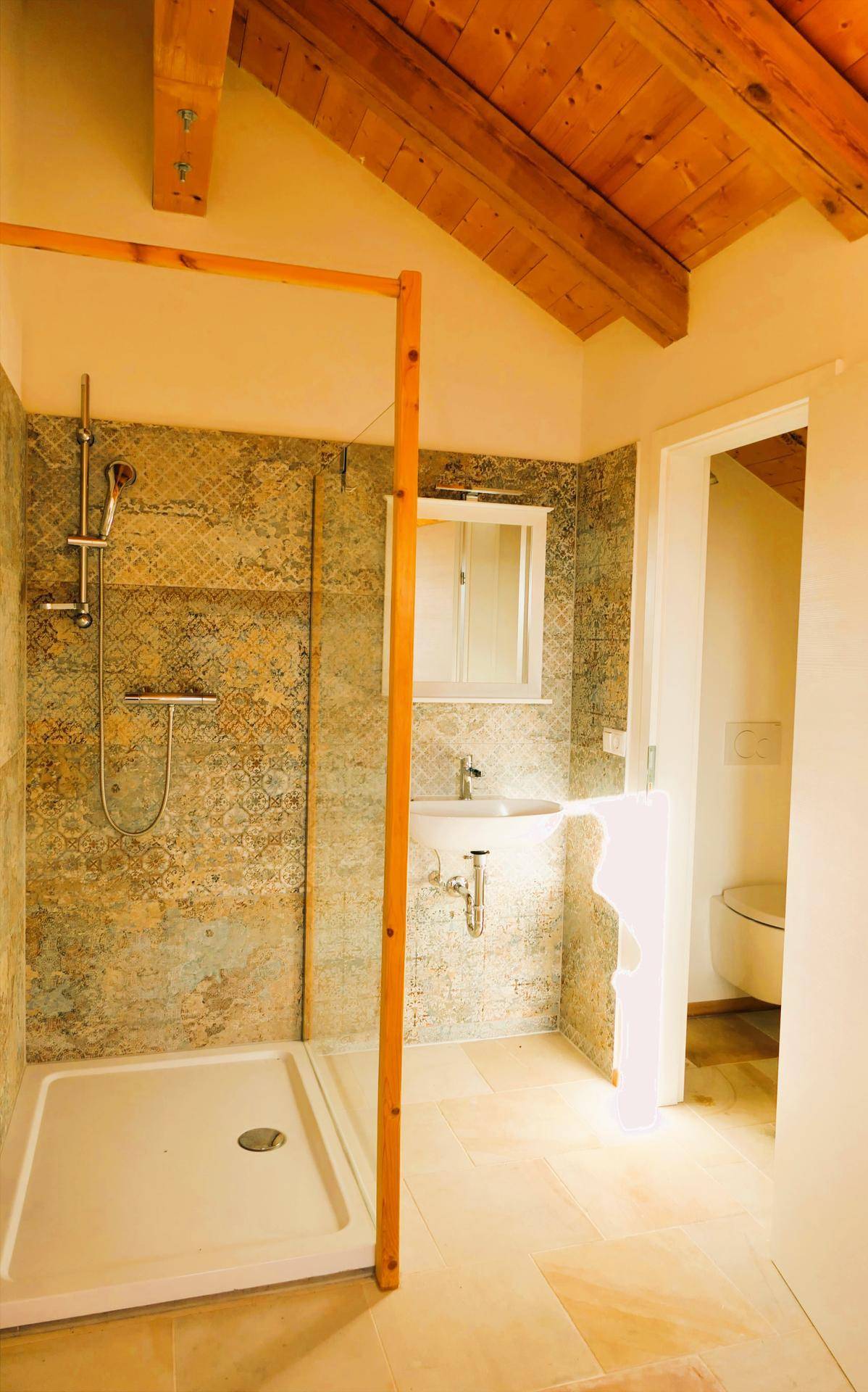 Helles Badezimmer mit Duschbereich, Waschbecken und gemusterten Fliesen an den Wänden.