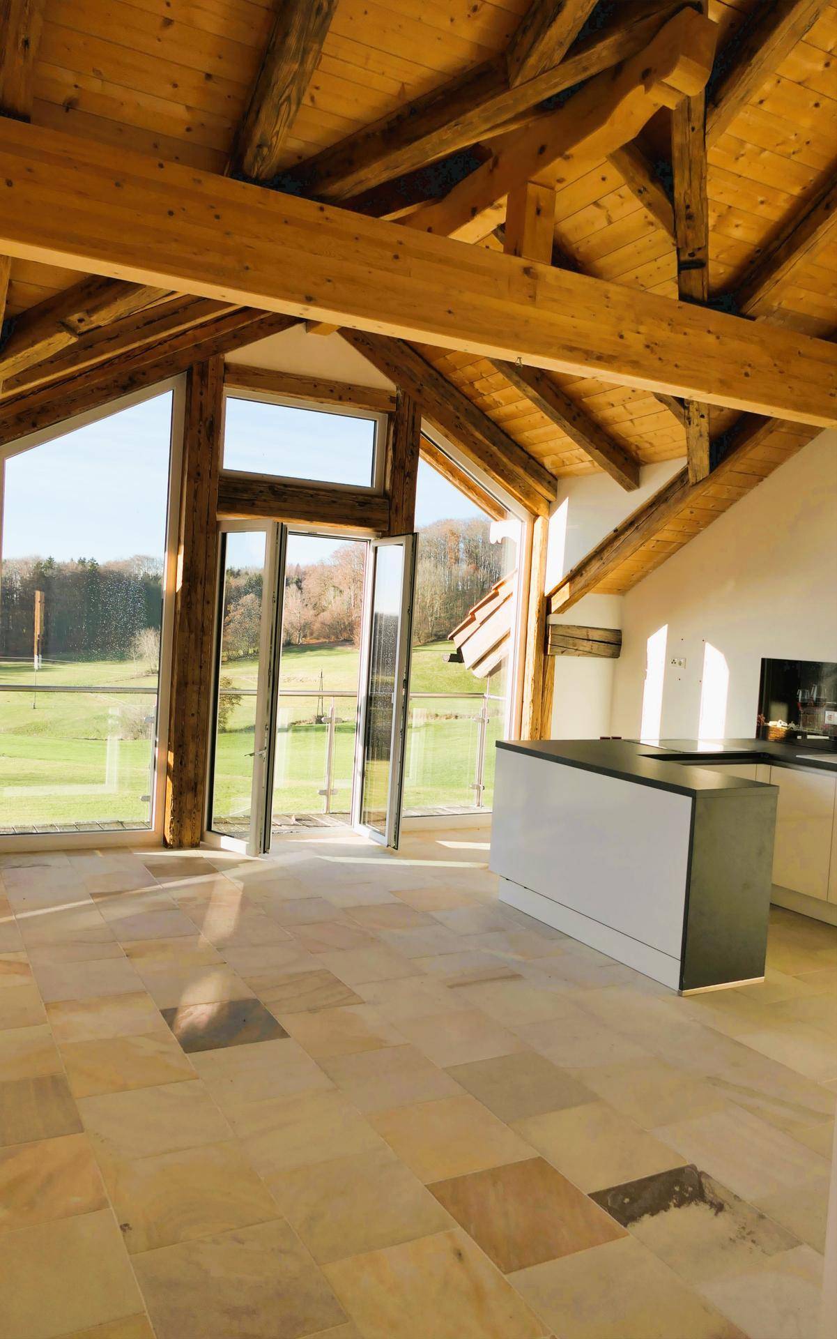 Offener Wohnbereich mit hohen Holzdecken, großen Fenstern und einer Kücheninsel mit weitem Ausblick.