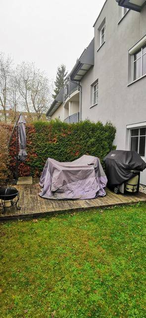 Gepflegter Gartenbereich mit Holzterrasse, hoher Hecke und überdachten Gartenmöbeln und Grill.