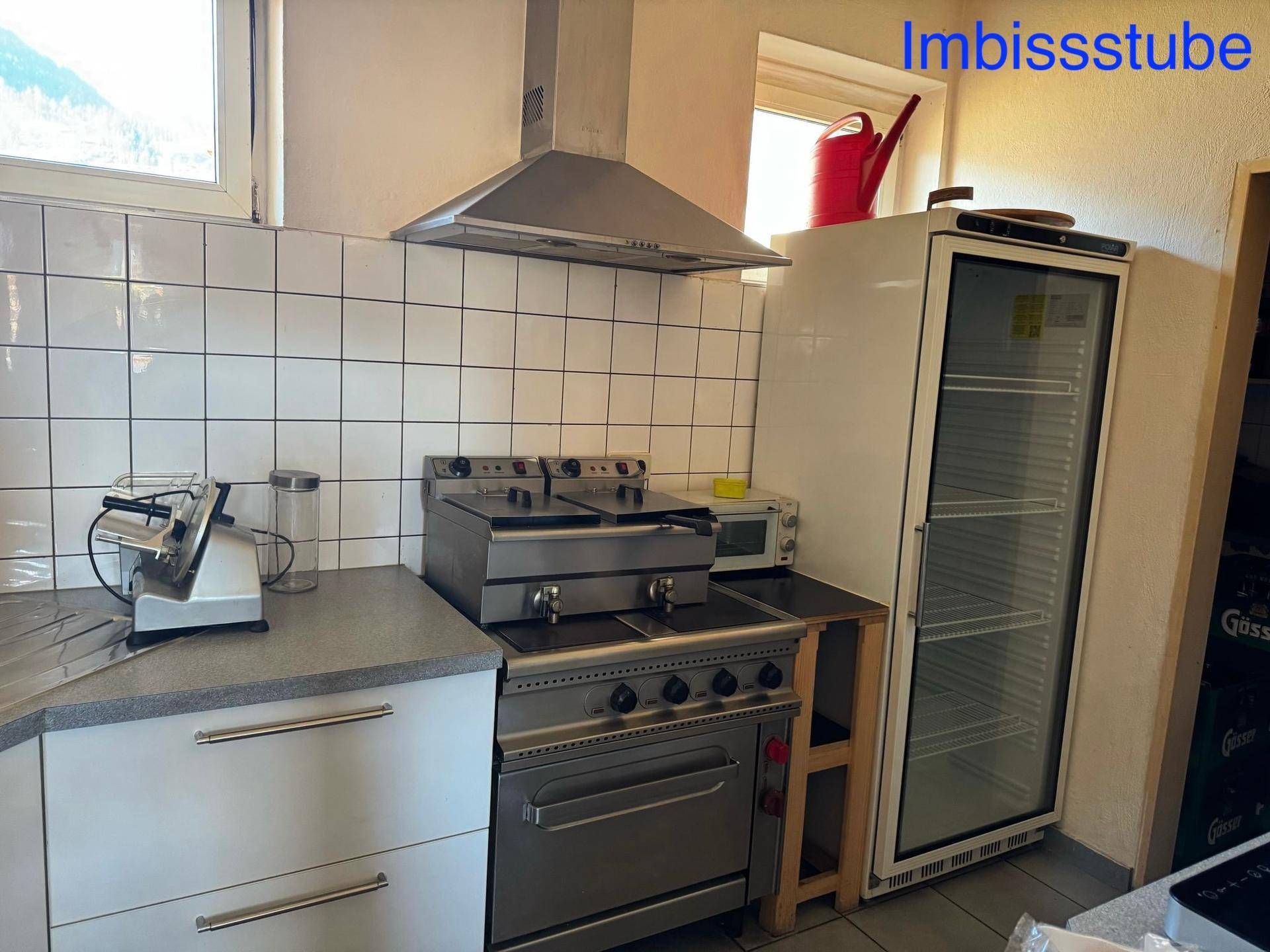 Professionelle Küche eines Imbisslokals mit Fritteusen, Herd und großem Kühlschrank.