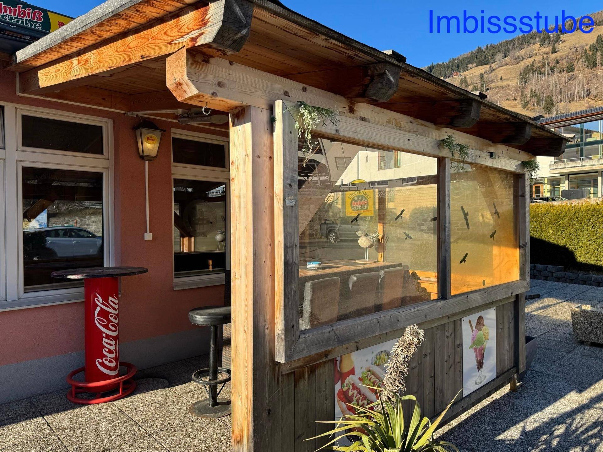 Seitenansicht der überdachten Terrasse eines Imbisslokals mit Holzelementen und Blick auf die Berge.