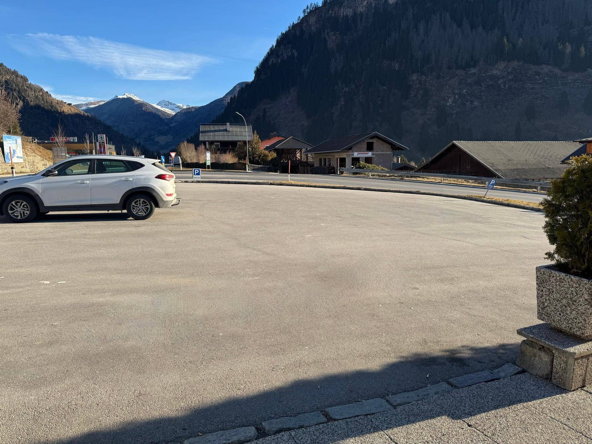 Großer asphaltierter Parkplatz vor einer Bergkulisse mit einem geparkten weißen Auto.