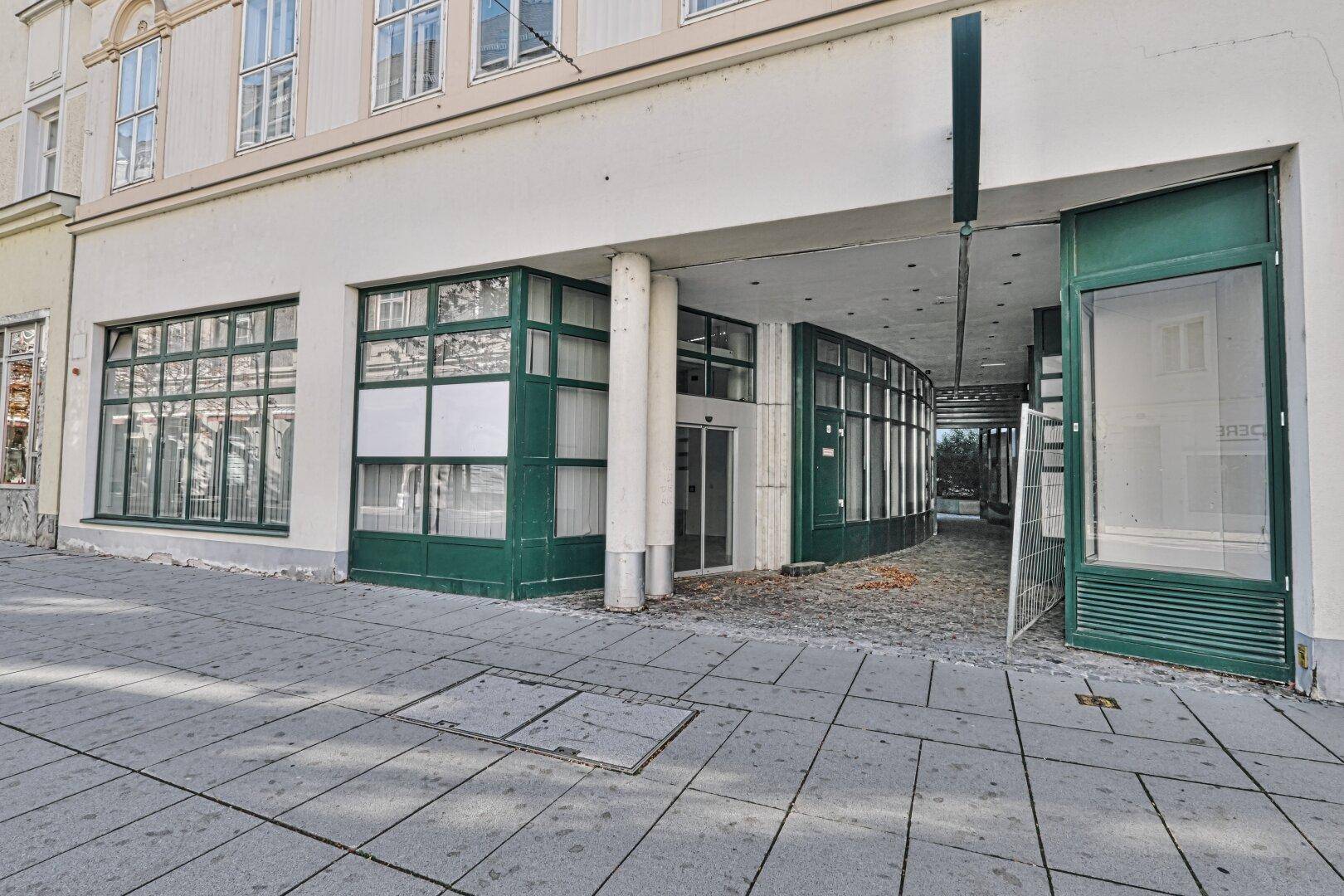Eingangsbereich eines Geschäftsgebäudes mit großen Schaufenstern und einem Durchgang zur Passage.