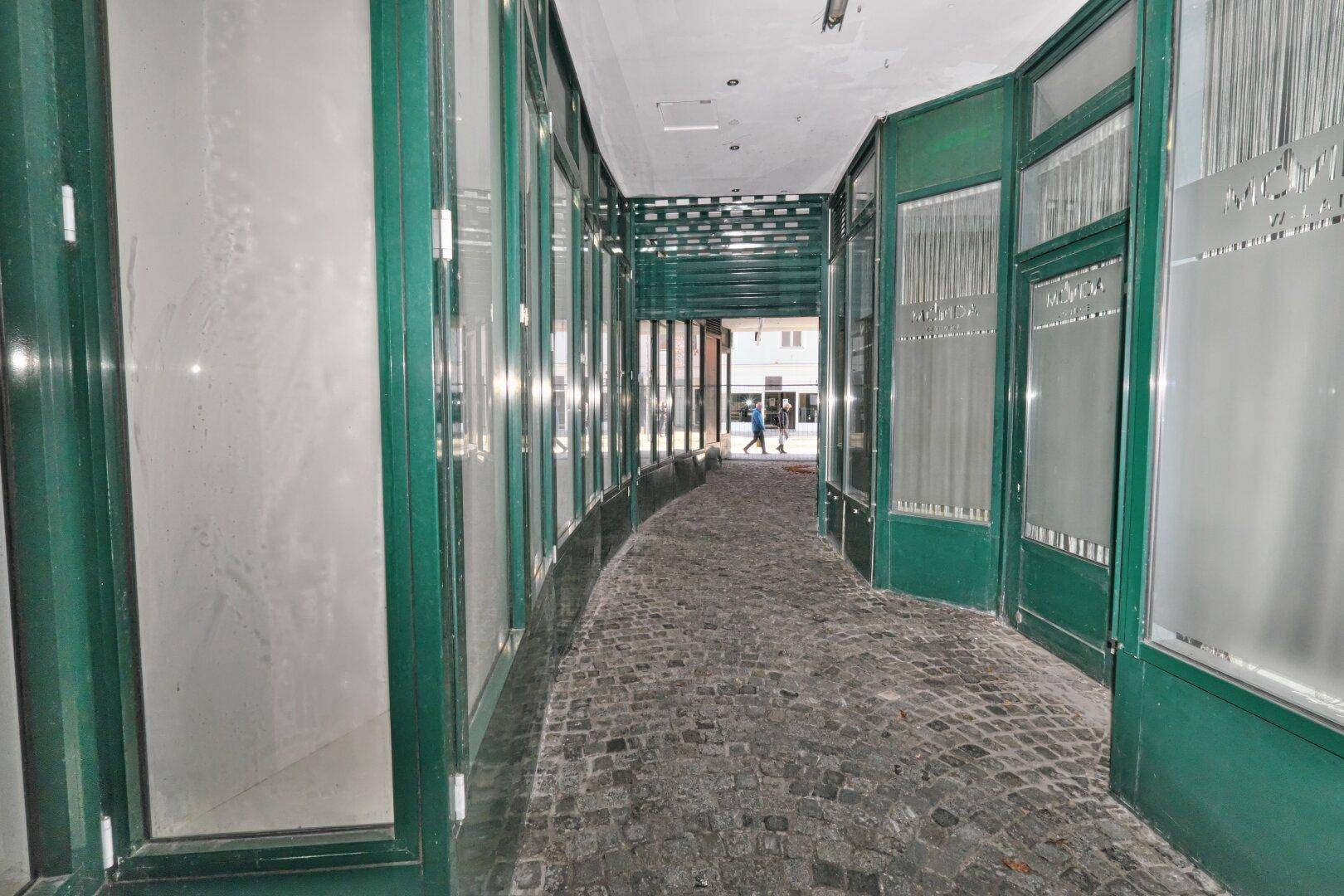 Lange, gewölbte Ladenpassage mit Kopfsteinpflaster und vielen Schaufenstern auf beiden Seiten.