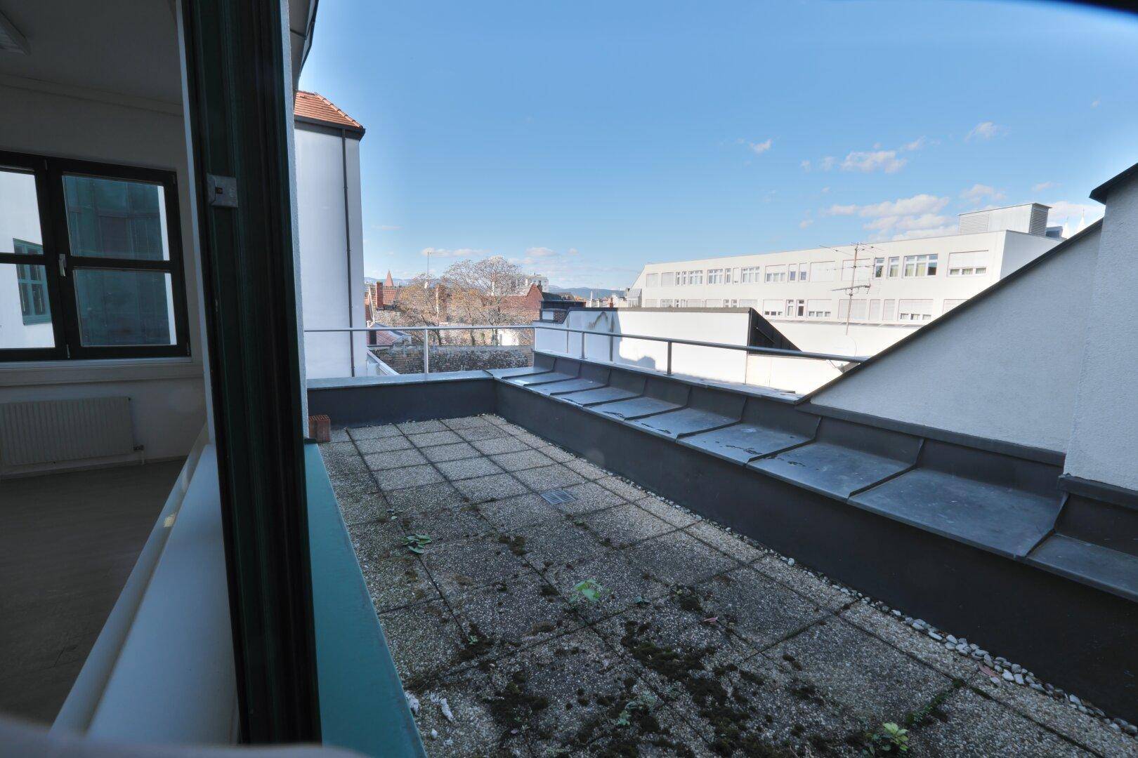 Große Dachterrasse mit Fliesenboden und Metallgeländer, bietet einen weiten Blick über die Stadt.