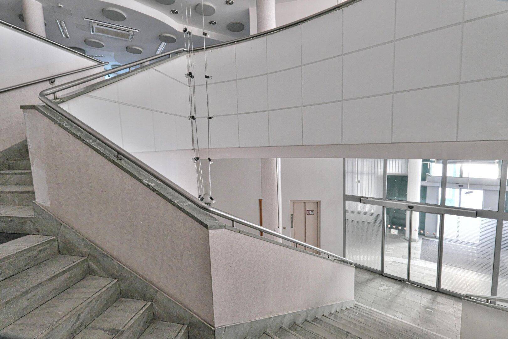 Breite Treppe mit Marmorstufen und Edelstahlgeländer, die zu verschiedenen Etagen führt.
